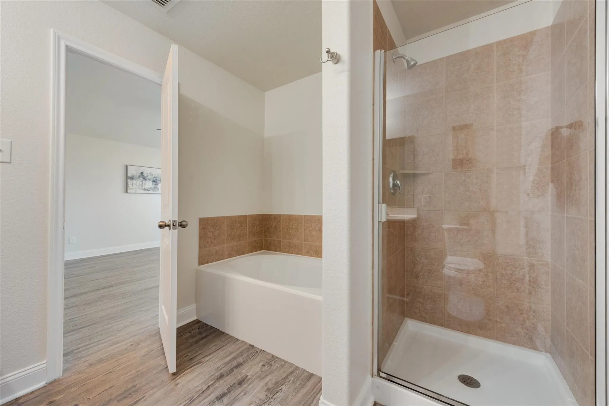 Walk-in shower with tiled surround and glass enclosure, soaking tub with tiled backsplash, and wood-finish flooring