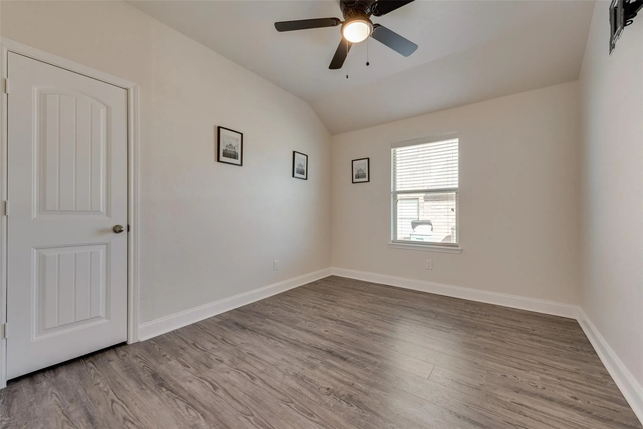 Wood-finish flooring, single window with blinds, ceiling fan with integrated lighting, white paneled door, and neutral wall tones