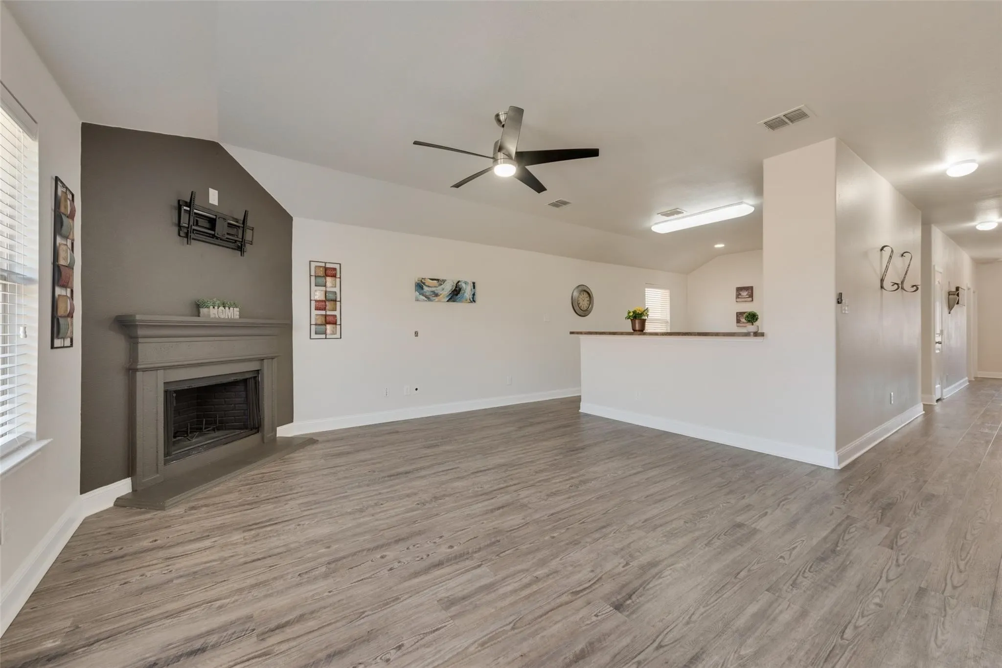 Wood-finish flooring throughout, fireplace with a mantel, vaulted ceiling, and an open-concept layout with a breakfast bar