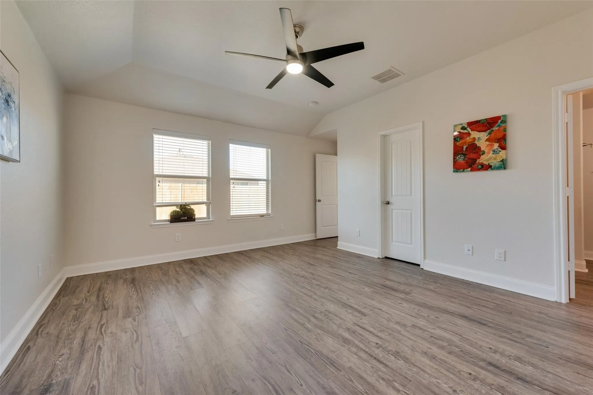 Vaulted ceiling, wood-finish flooring, three windows with blinds, ceiling fan, and white interior doors