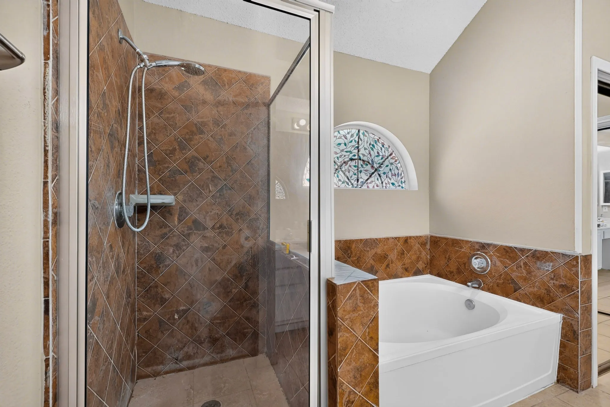 Glass-enclosed shower with tiled walls, separate soaking tub, and decorative arched window