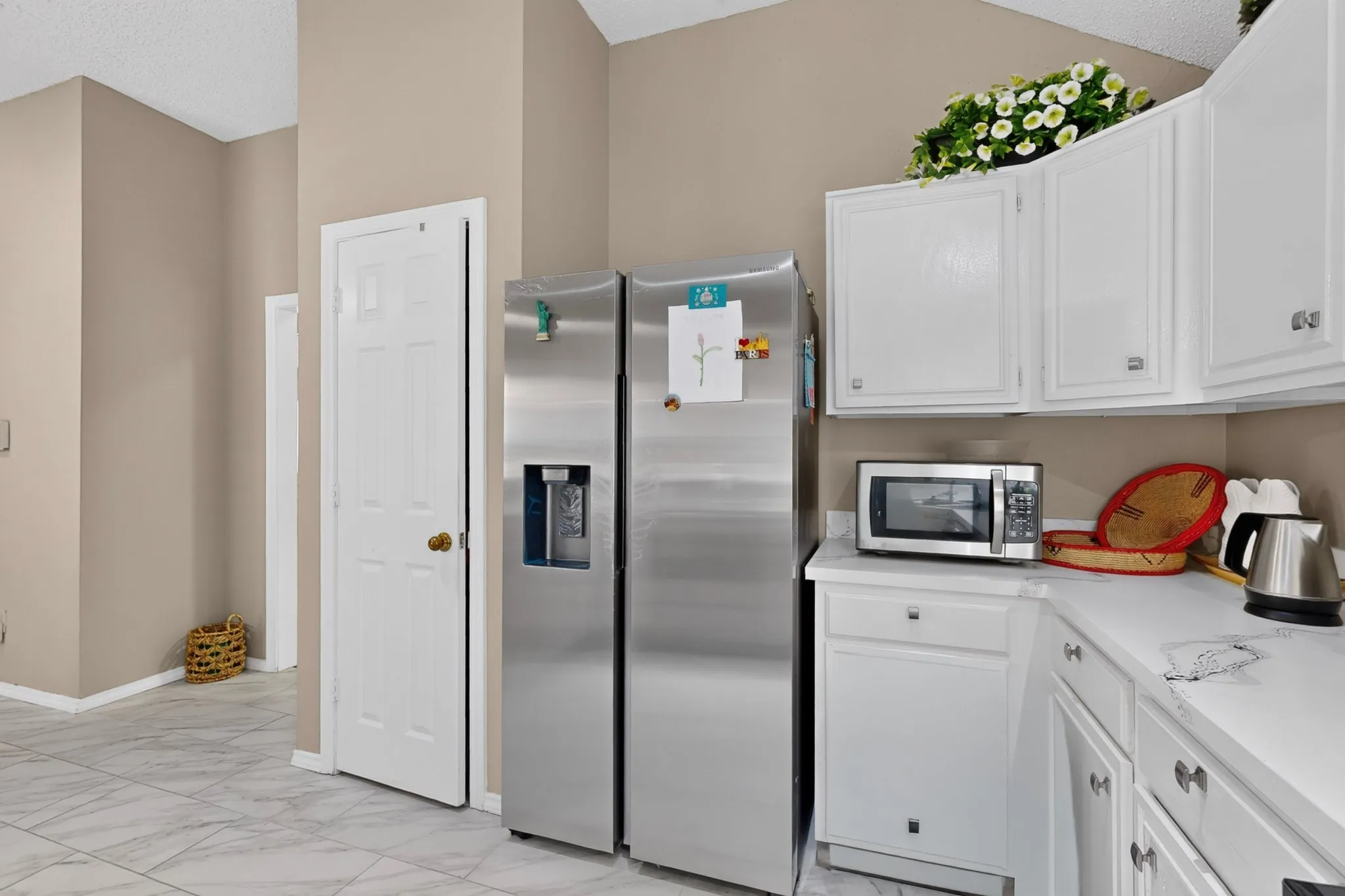 Built-in white cabinetry, stainless steel refrigerator, white countertops, and light-toned tile flooring