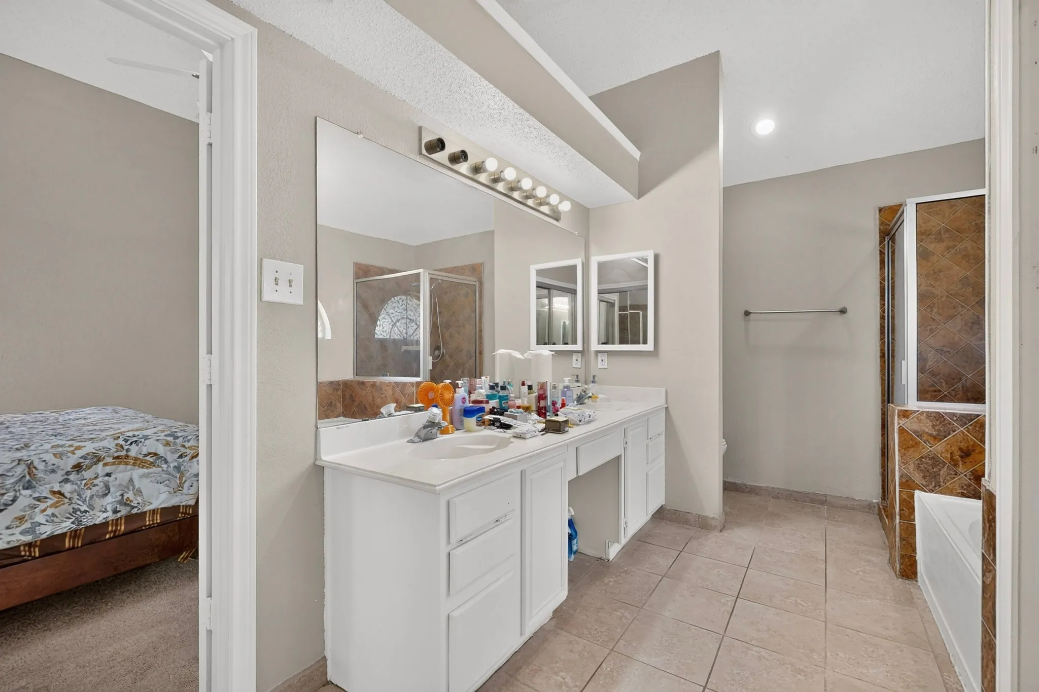 Dual vanity with white cabinetry, tile flooring, built-in bathtub, and a separate tiled shower enclosure