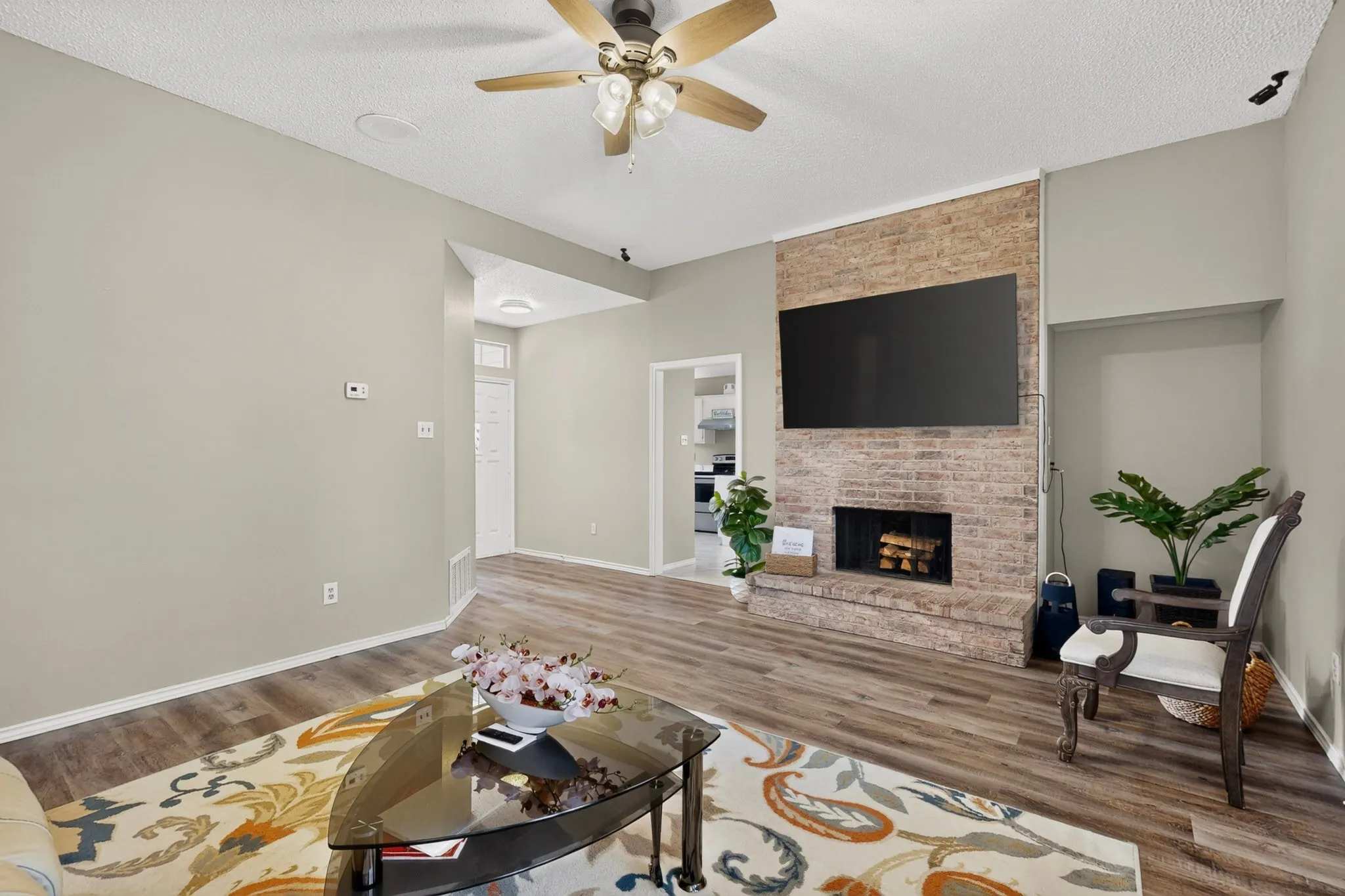 Brick-faced fireplace with a hearth, wood-finish flooring, and a ceiling fan with integrated lighting
