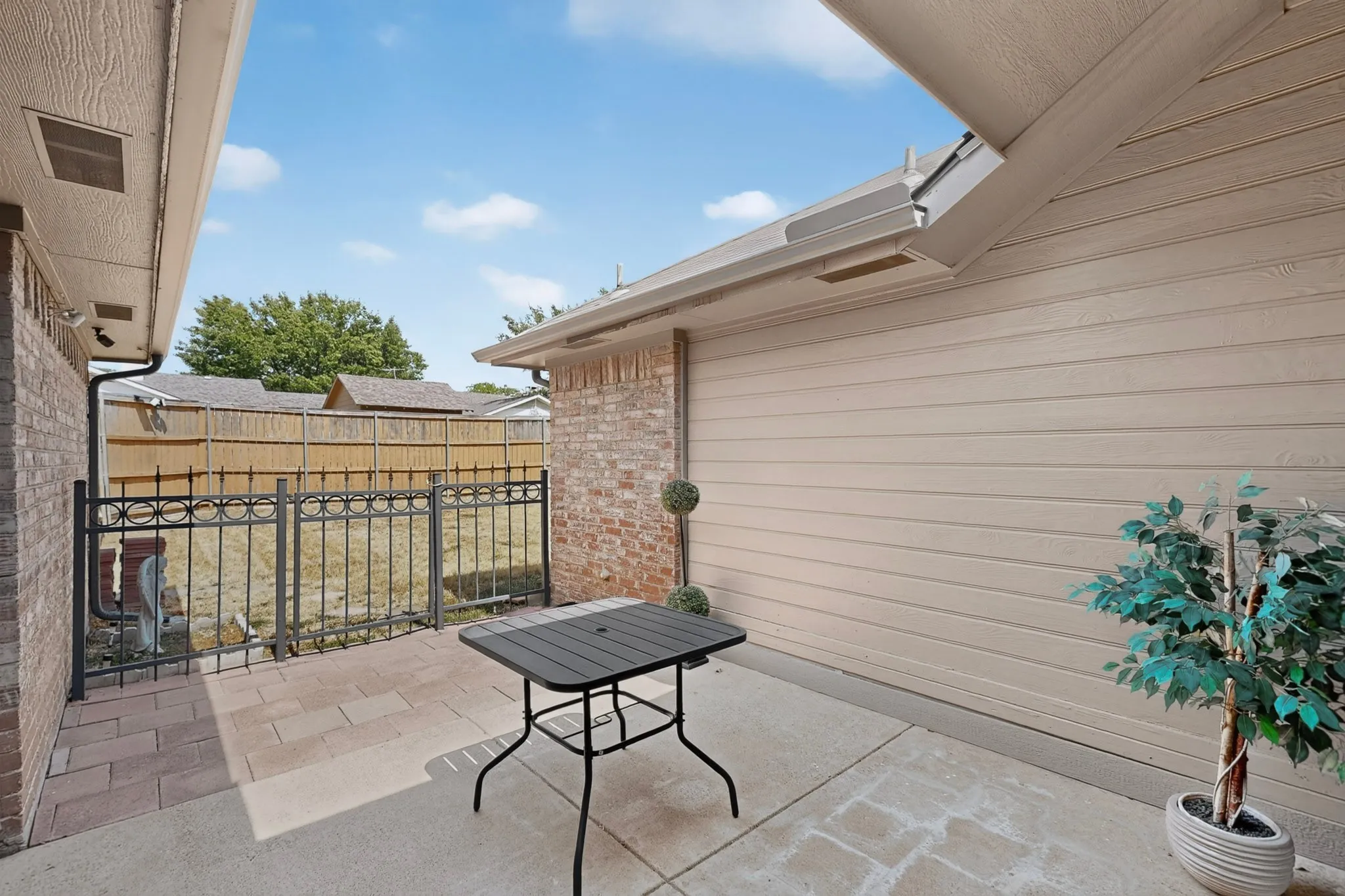 Paved patio area featuring brick siding and horizontal plank siding, with a wrought iron fence and wood privacy fence