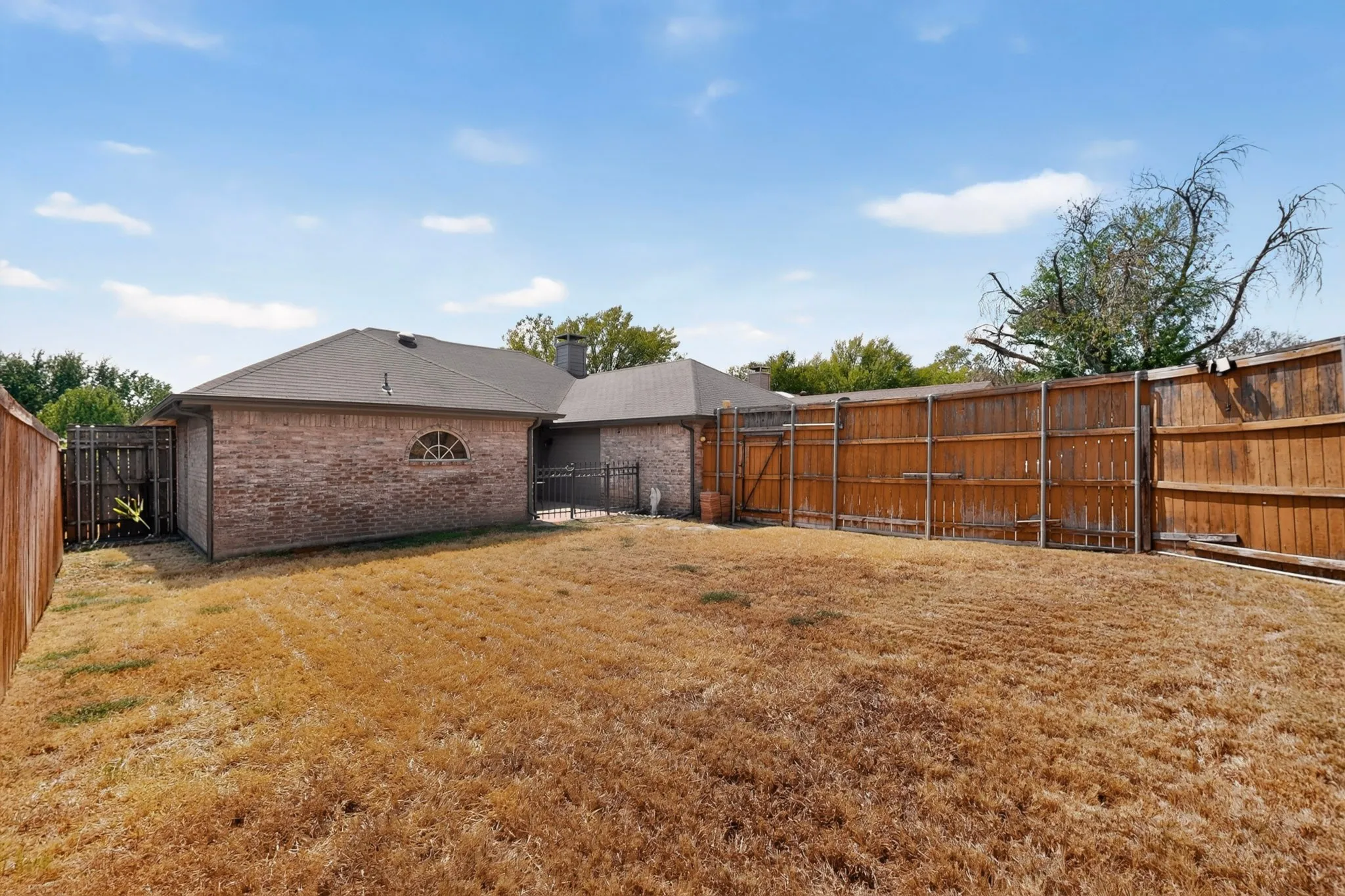 Brick exterior with a half-round decorative window, surrounded by a wood privacy fence