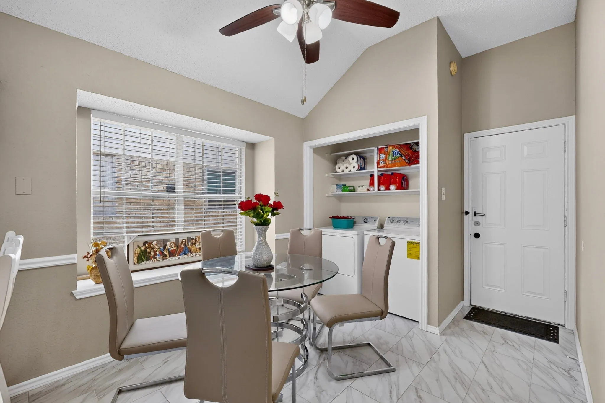 Vaulted ceilings with a ceiling fan, a window with horizontal blinds, built-in laundry area with shelving, and light-toned tile flooring