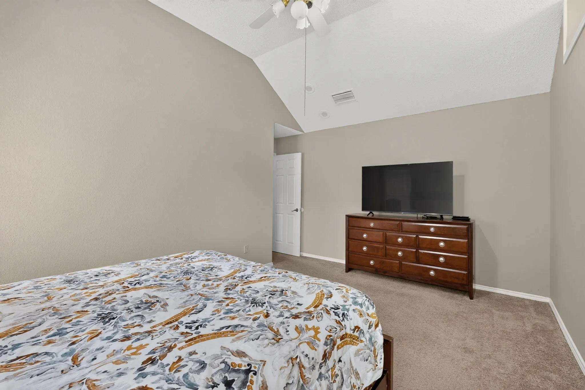 Vaulted ceiling, ceiling fan, neutral wall paint, carpet flooring, interior door