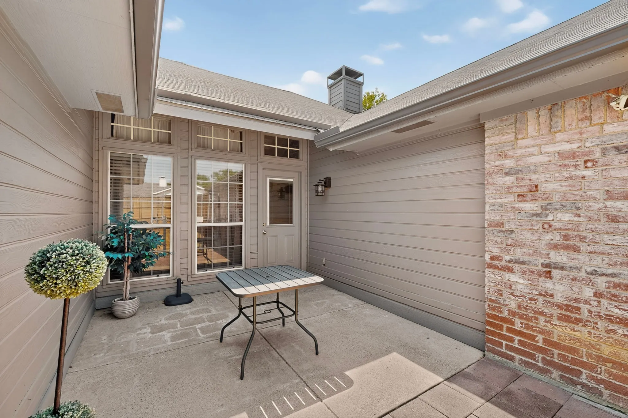 Concrete patio with brick and siding exterior, featuring multiple windows and a door with transom lites