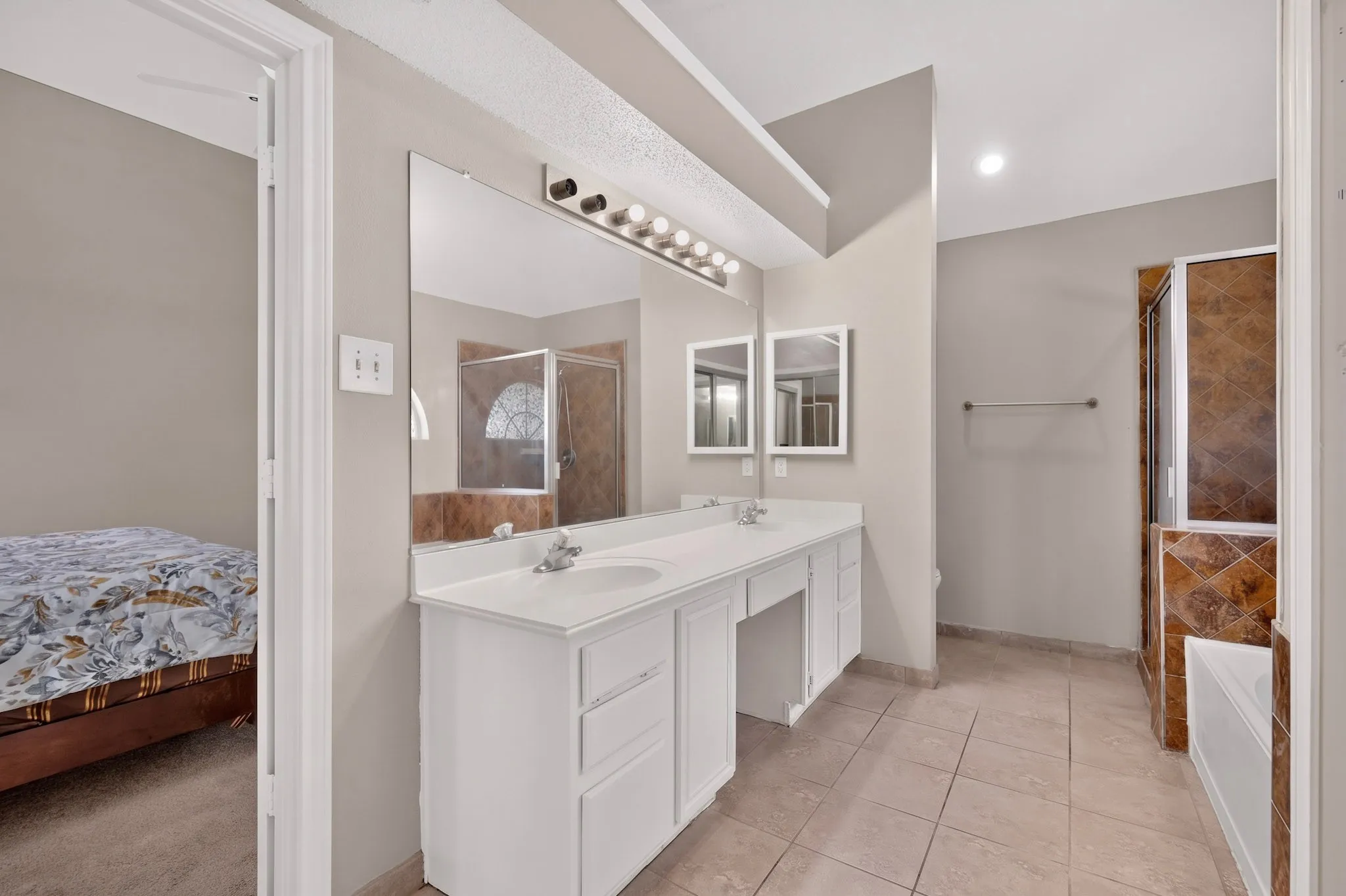 Dual sink vanity with white cabinetry, large vanity mirror, tile flooring, and a walk-in shower with glass enclosure