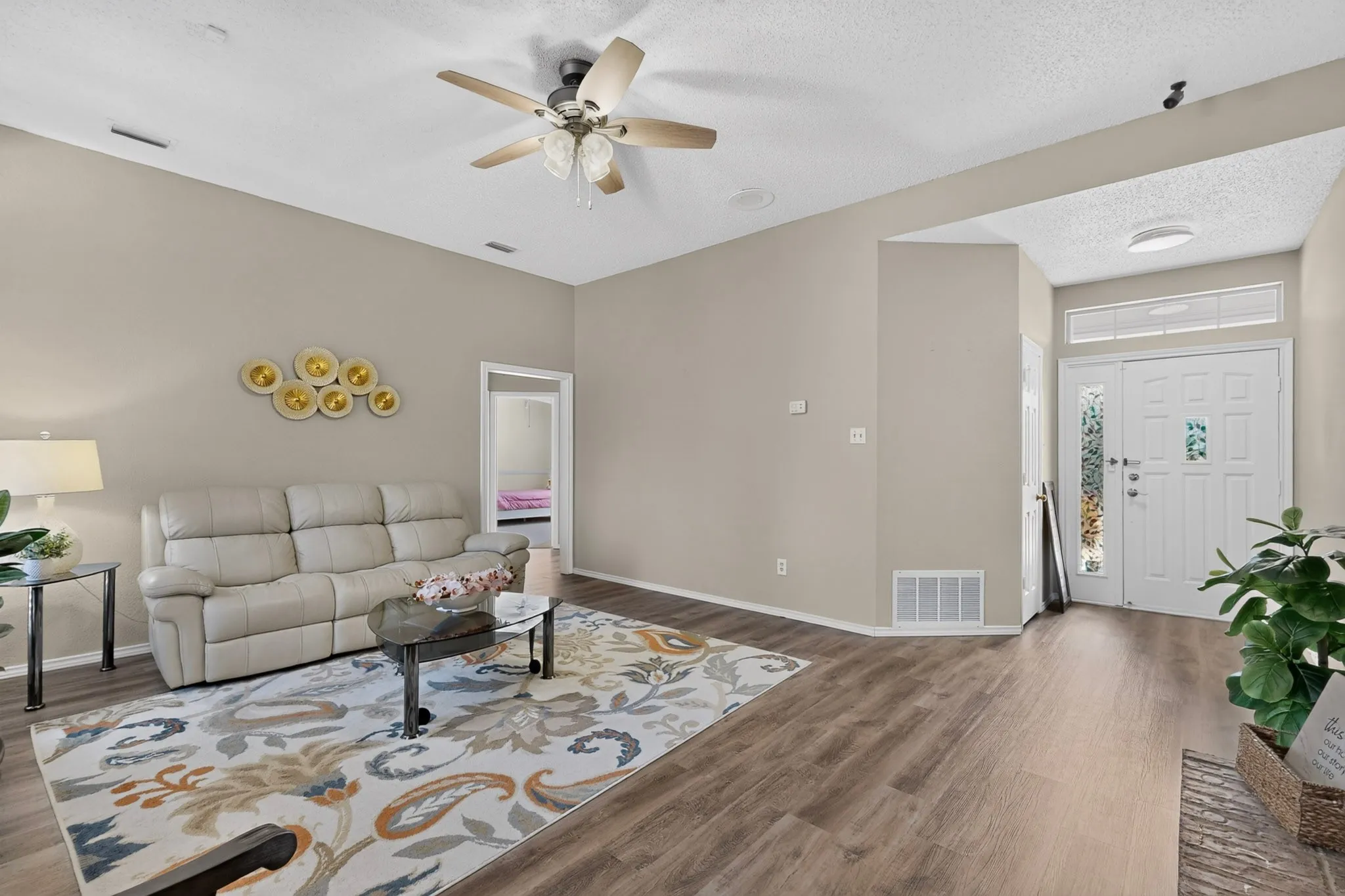 Vaulted ceiling, wood-finish flooring, ceiling fan, white paneled entry door with decorative glass inserts, and transom window