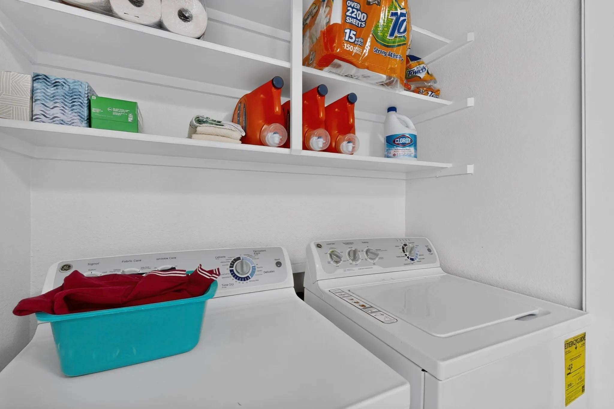 White washer and dryer units, white wall-mounted shelving, and white walls