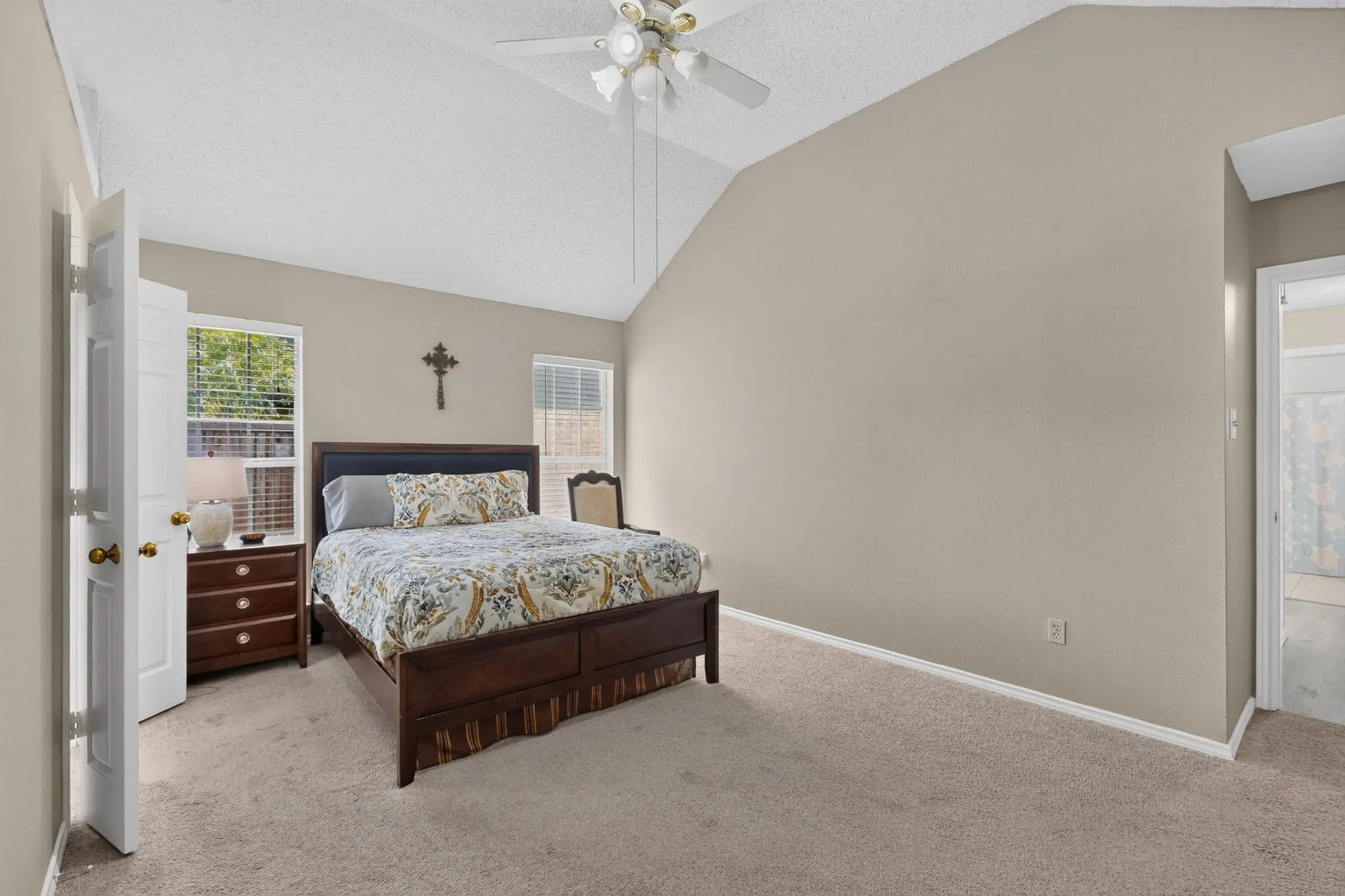 Vaulted ceiling, ceiling fan, carpet flooring, two windows with blinds, and a white paneled door