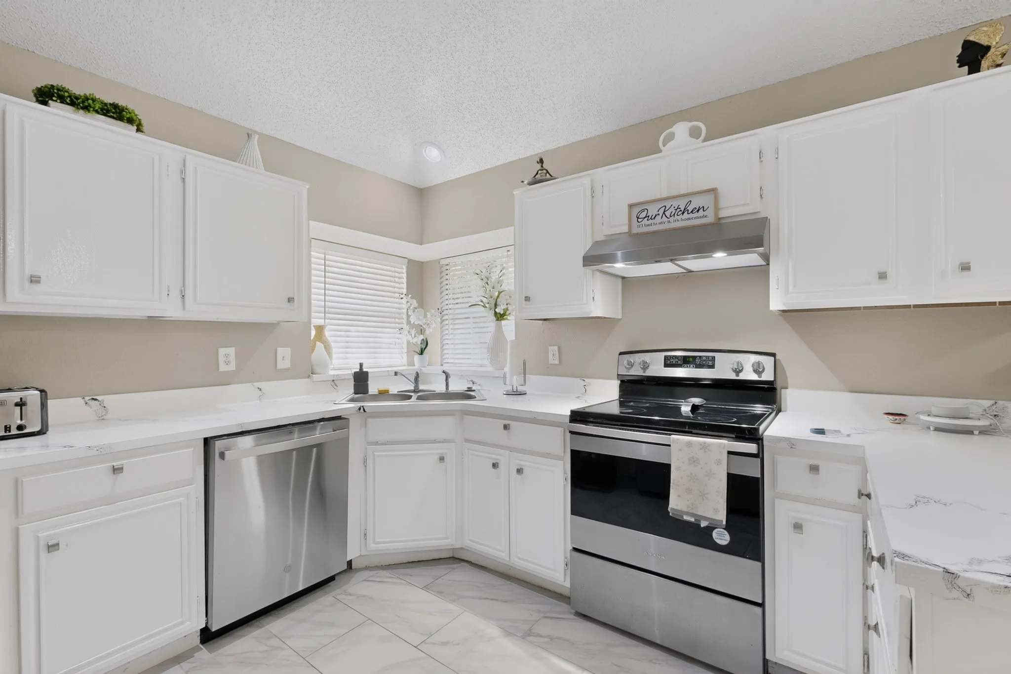 White cabinetry with brushed nickel hardware, stainless steel appliances, light-toned countertops, and tiled flooring