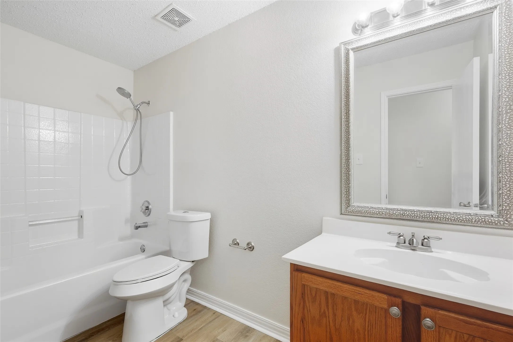 Wood-finish flooring with white baseboards, a white tub and shower combination with tile surround, and a wood vanity with a white countertop and integrated sink