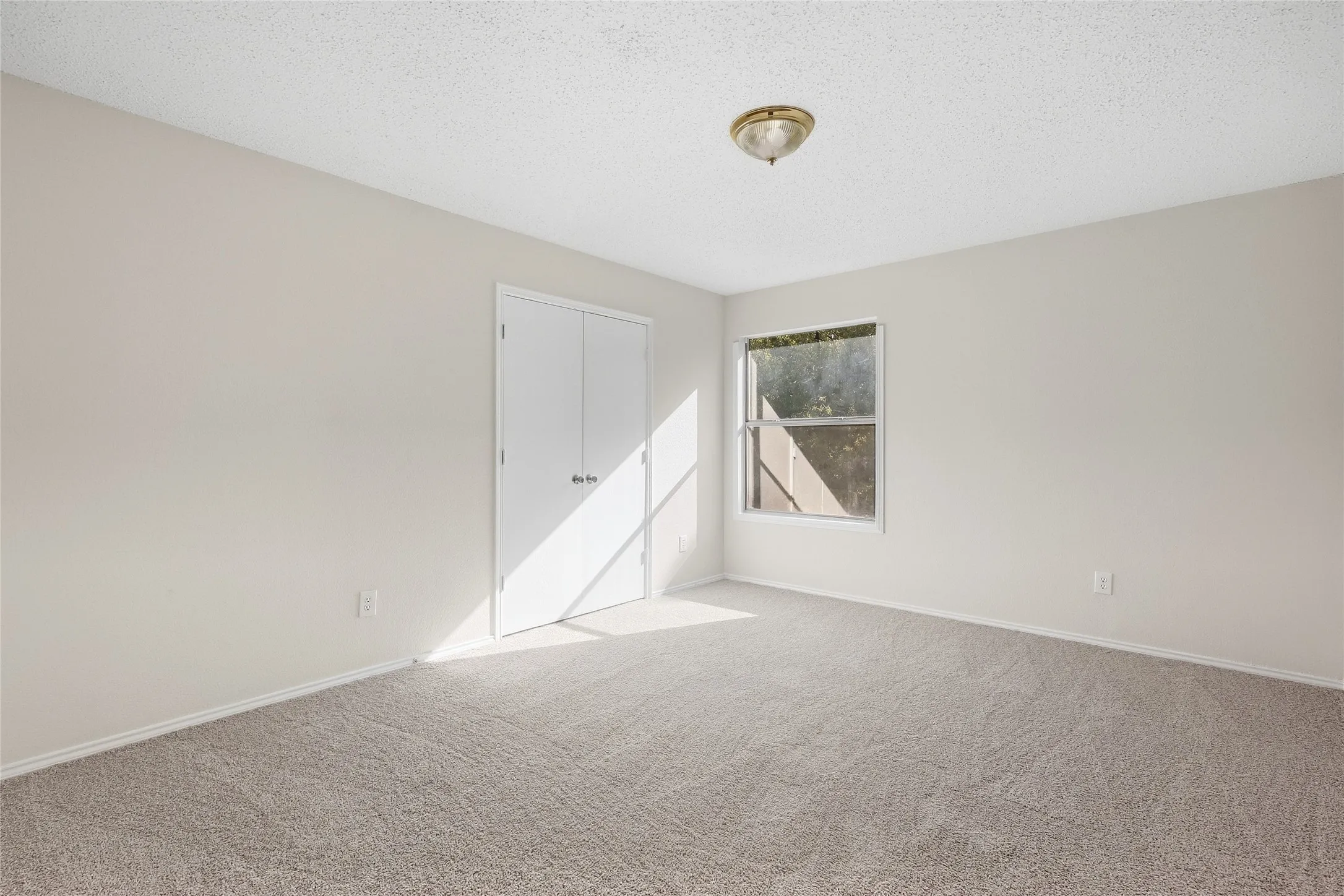 Neutral wall paint, textured ceiling, flush mount ceiling light, dual closet doors, and light-toned carpet