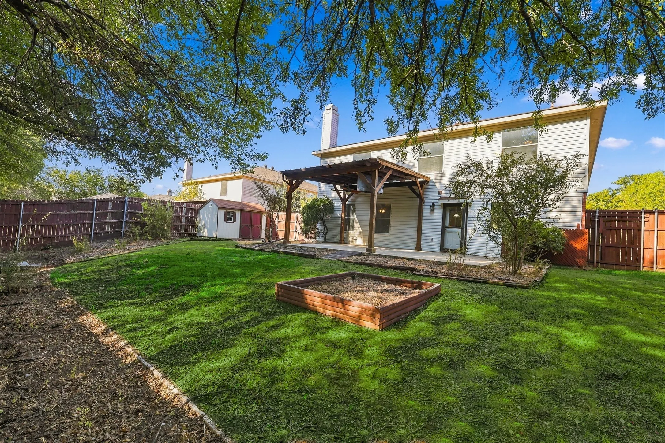 Expansive backyard featuring a wood pergola, concrete patio, garden bed, and a storage shed