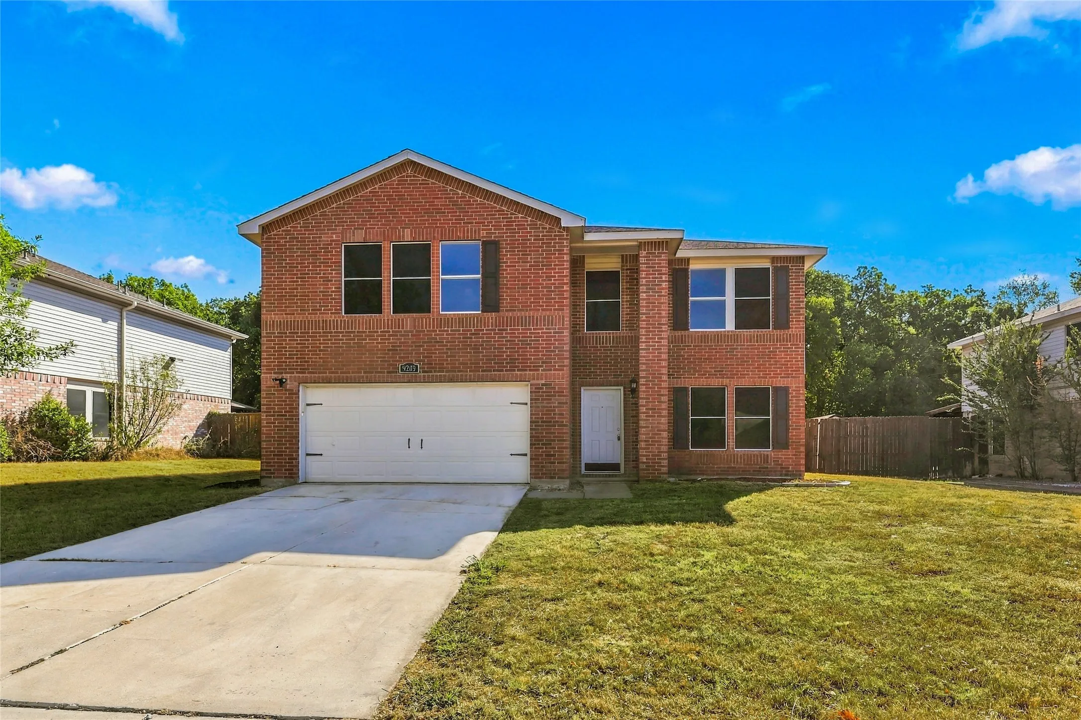 Brick exterior with a prominent two-car garage, multiple windows with dark shutters, and a concrete driveway