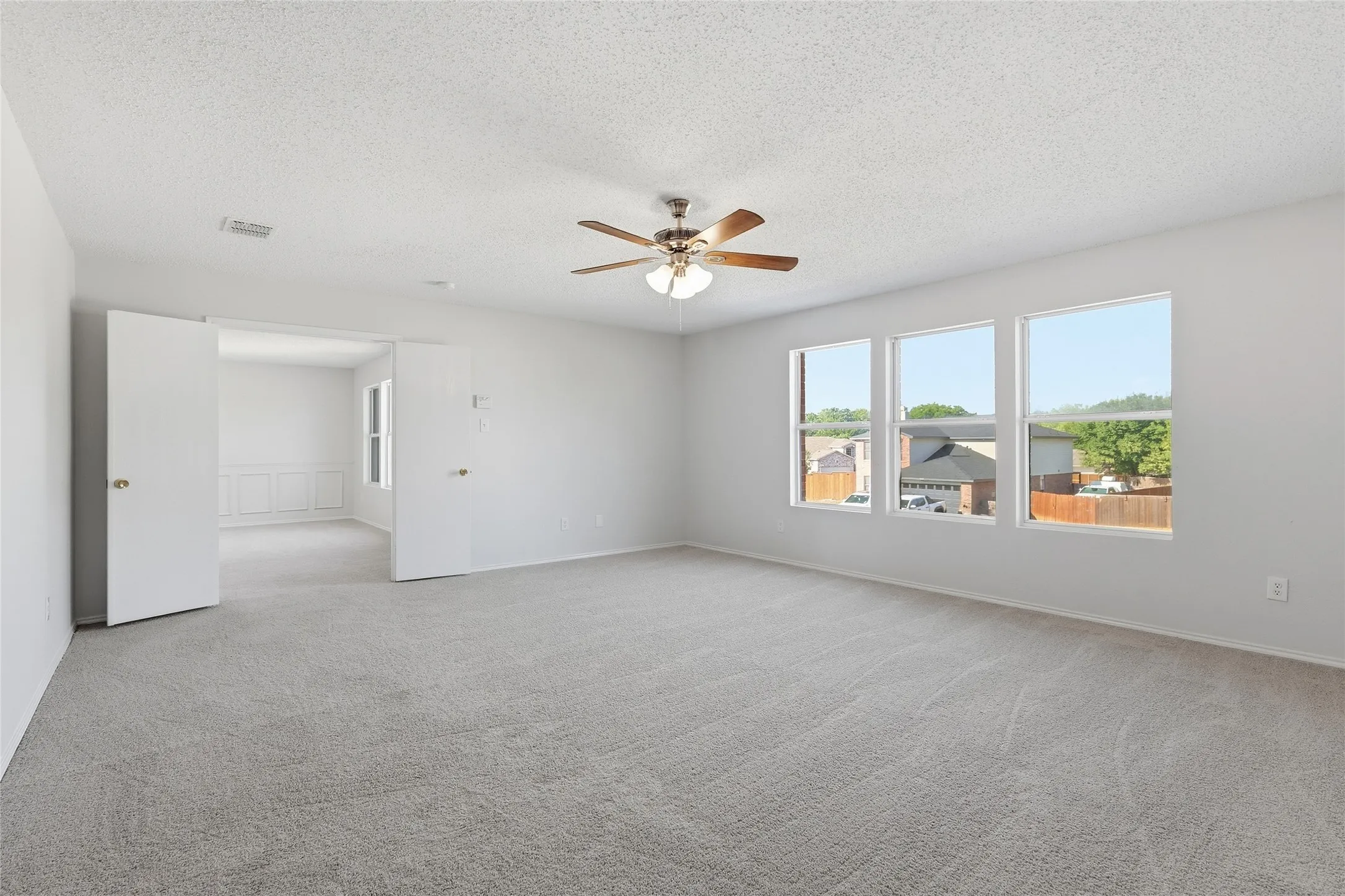 Expansive room with neutral carpet, three large windows, and a ceiling fan