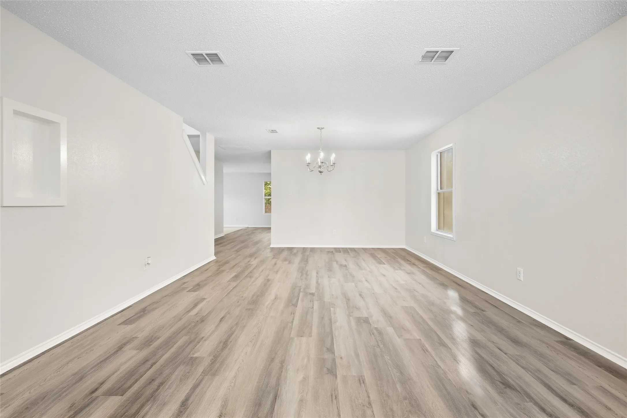 Wood-finish flooring throughout, white painted walls, and a multi-arm chandelier