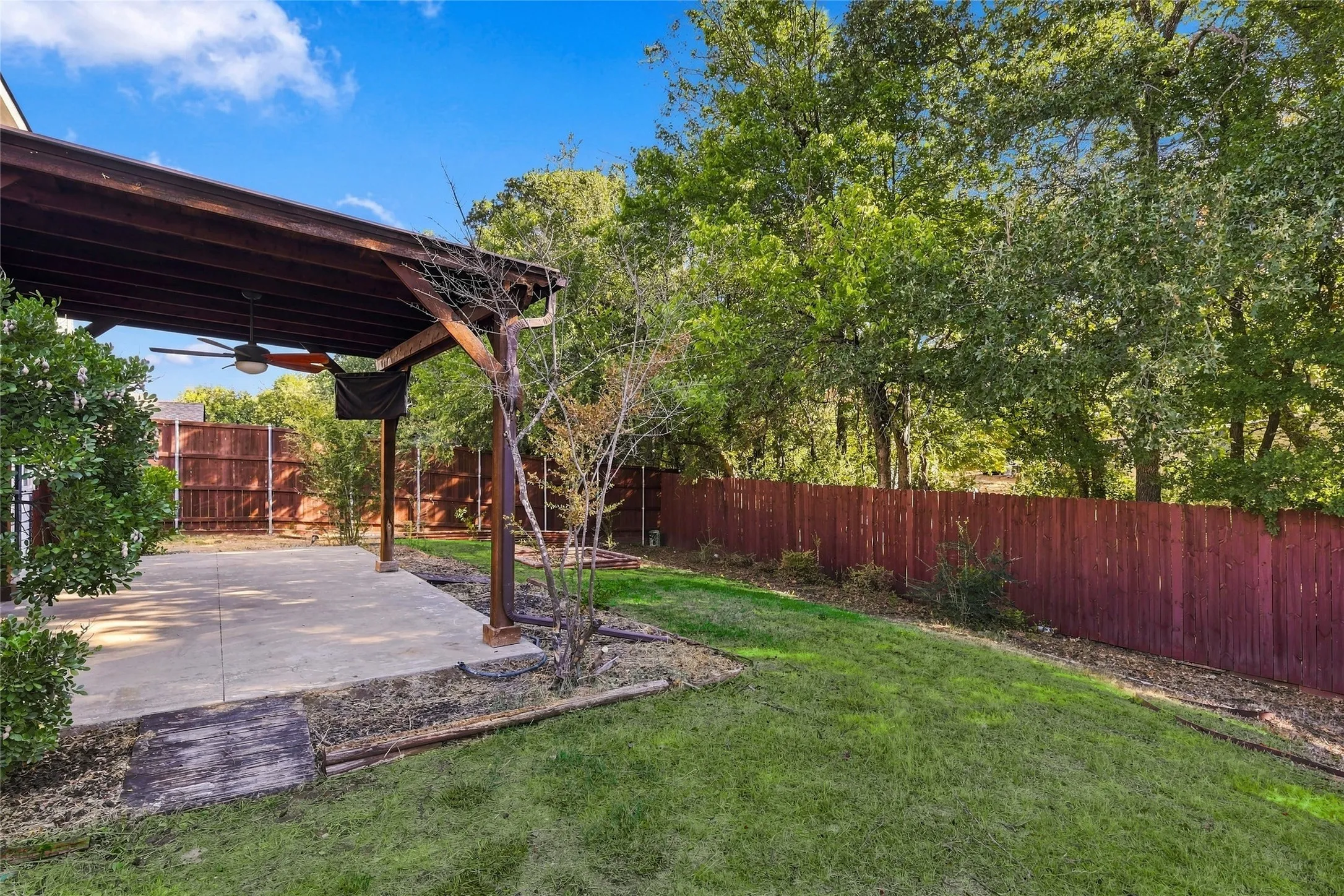 Covered patio with a ceiling fan, concrete surface, and a stained wood privacy fence
