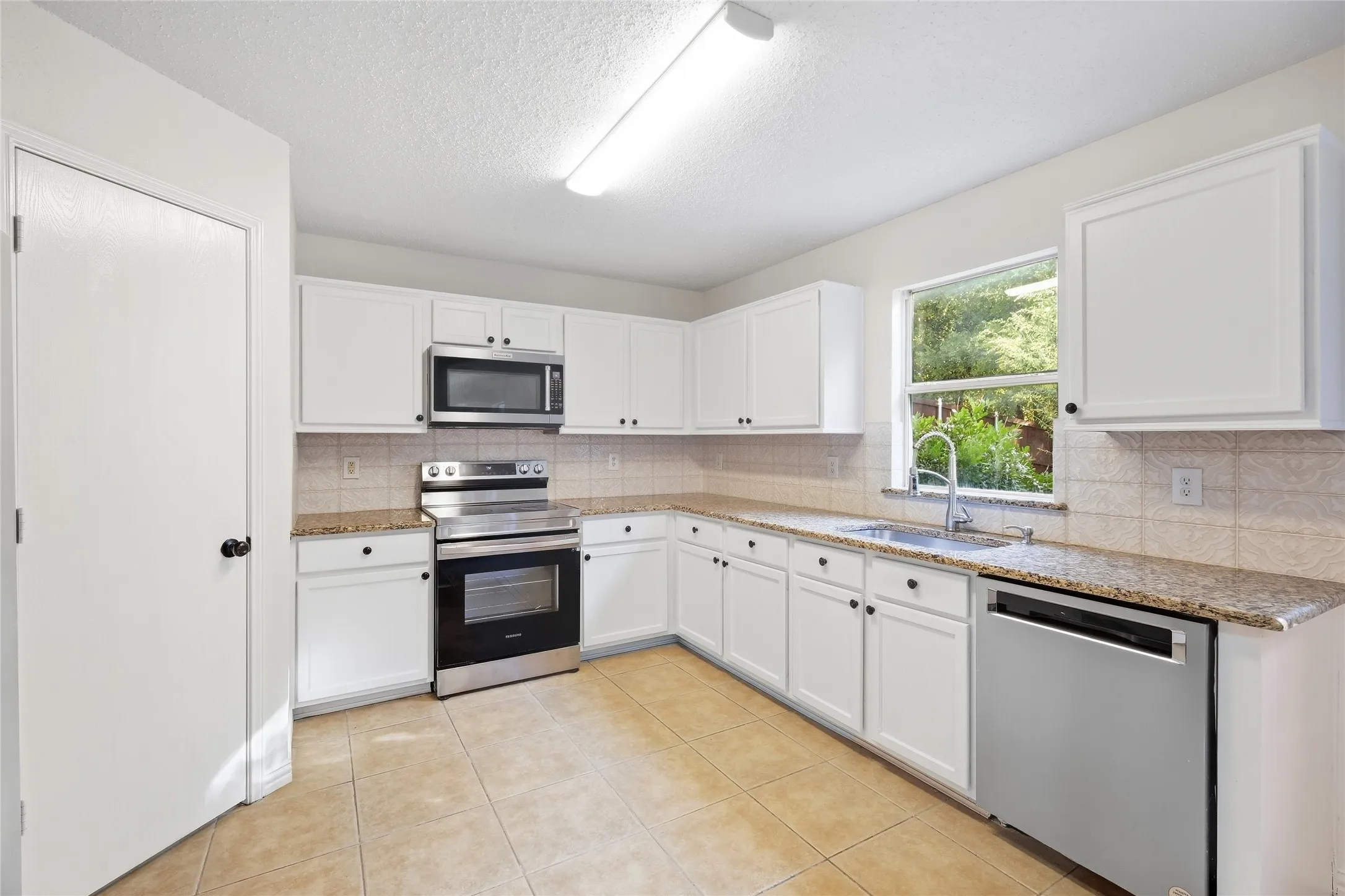 Kitchen featuring white cabinetry, granite countertops, stainless steel appliances, tile flooring, and a tile backsplash