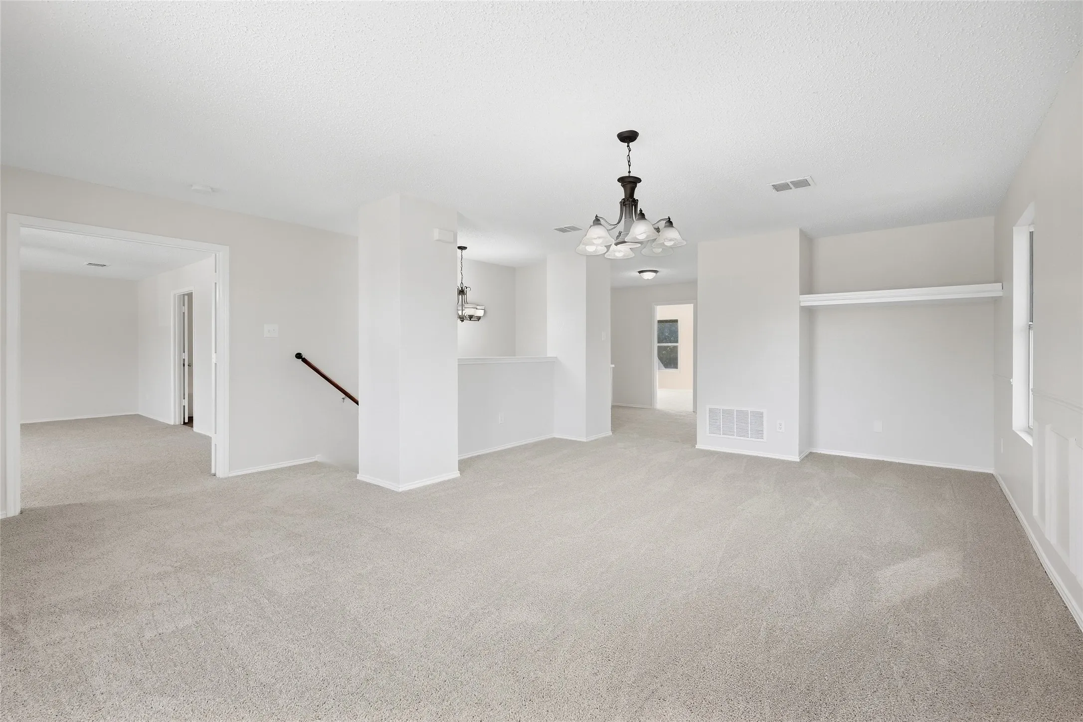 Expansive carpeted area with a decorative chandelier and white walls
