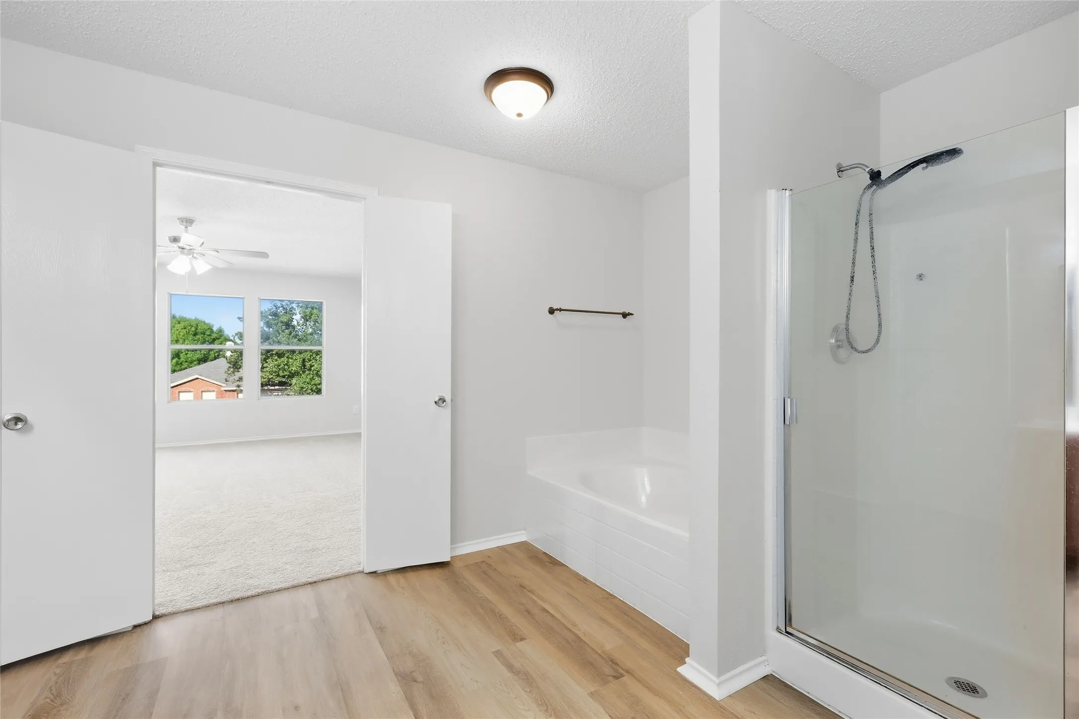 Walk-in shower with glass enclosure, soaking tub, and wood-finish flooring