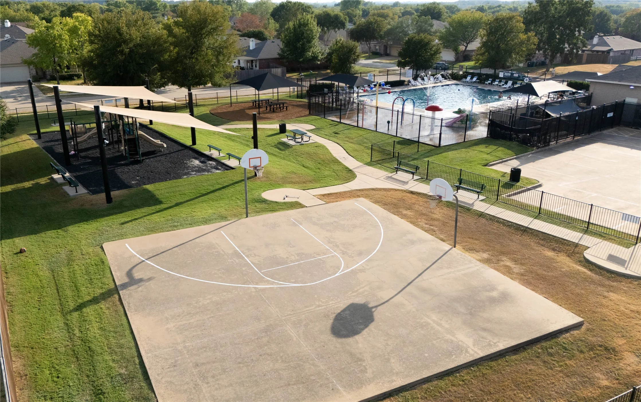 Outdoor basketball court, shaded playground structure with benches, fenced swimming pool, and dedicated splash pad area