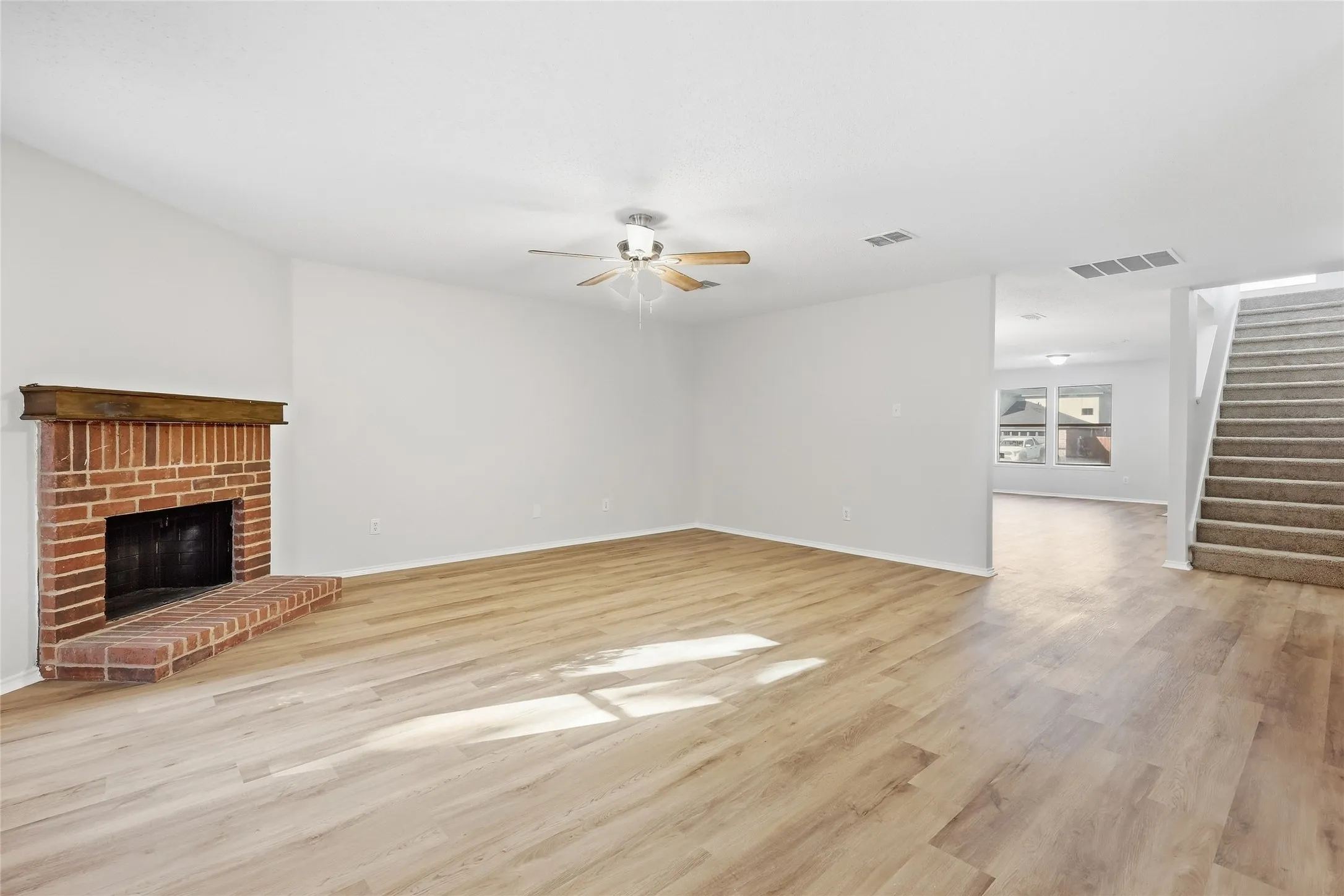 Brick fireplace with a wood mantel, wood-finish flooring, and a ceiling fan