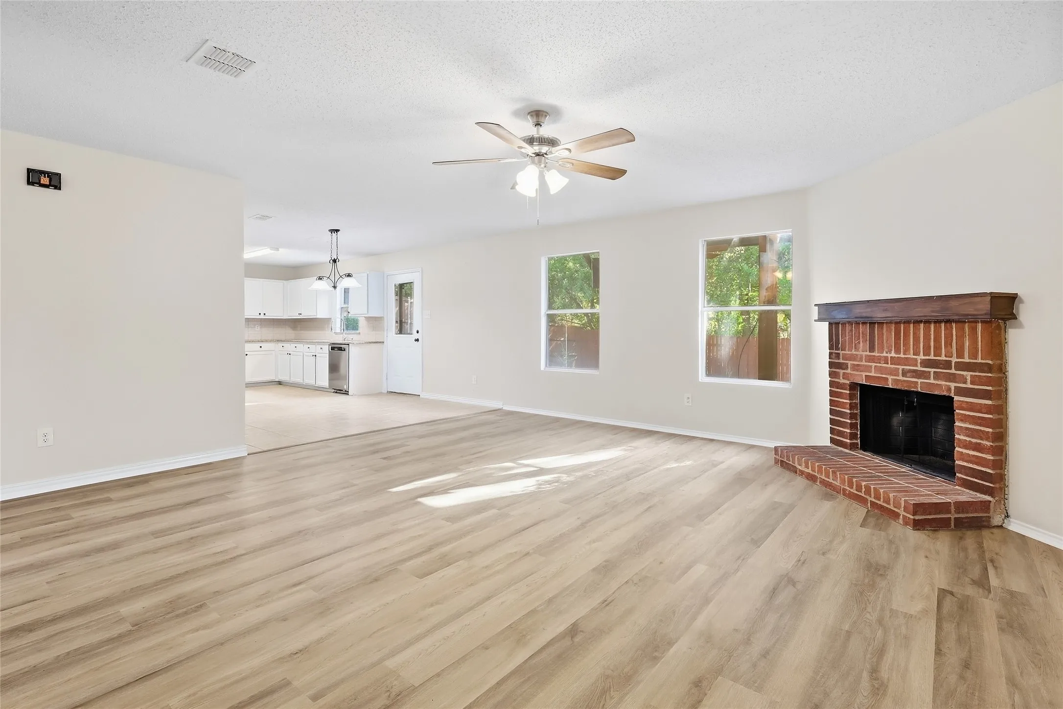 Spacious living area featuring wood-finish flooring, a brick fireplace with a wood mantle, and a ceiling fan