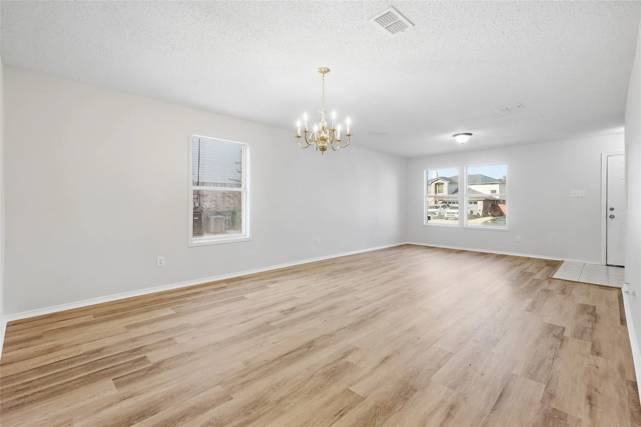 Spacious room featuring wood-finish flooring, multiple windows, a chandelier, and recessed lighting