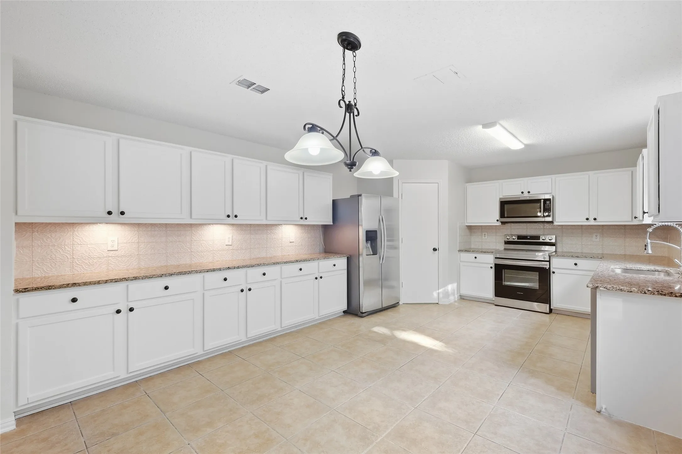 Spacious kitchen featuring white cabinetry, light-toned tile flooring, recessed under-cabinet lighting, and stainless steel appliances