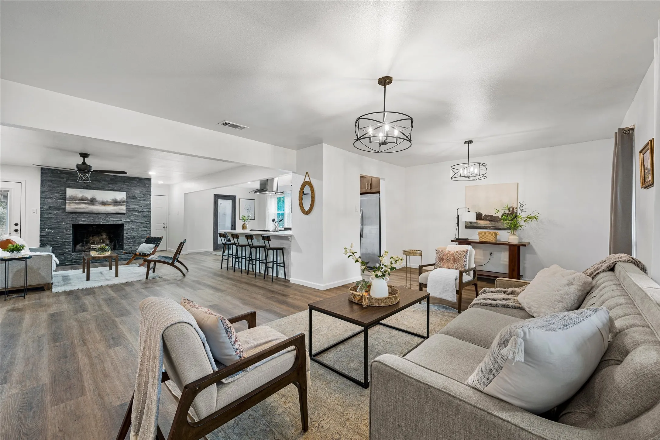 Spacious living area featuring wood-finish flooring, a stacked stone fireplace, and contemporary lighting fixtures