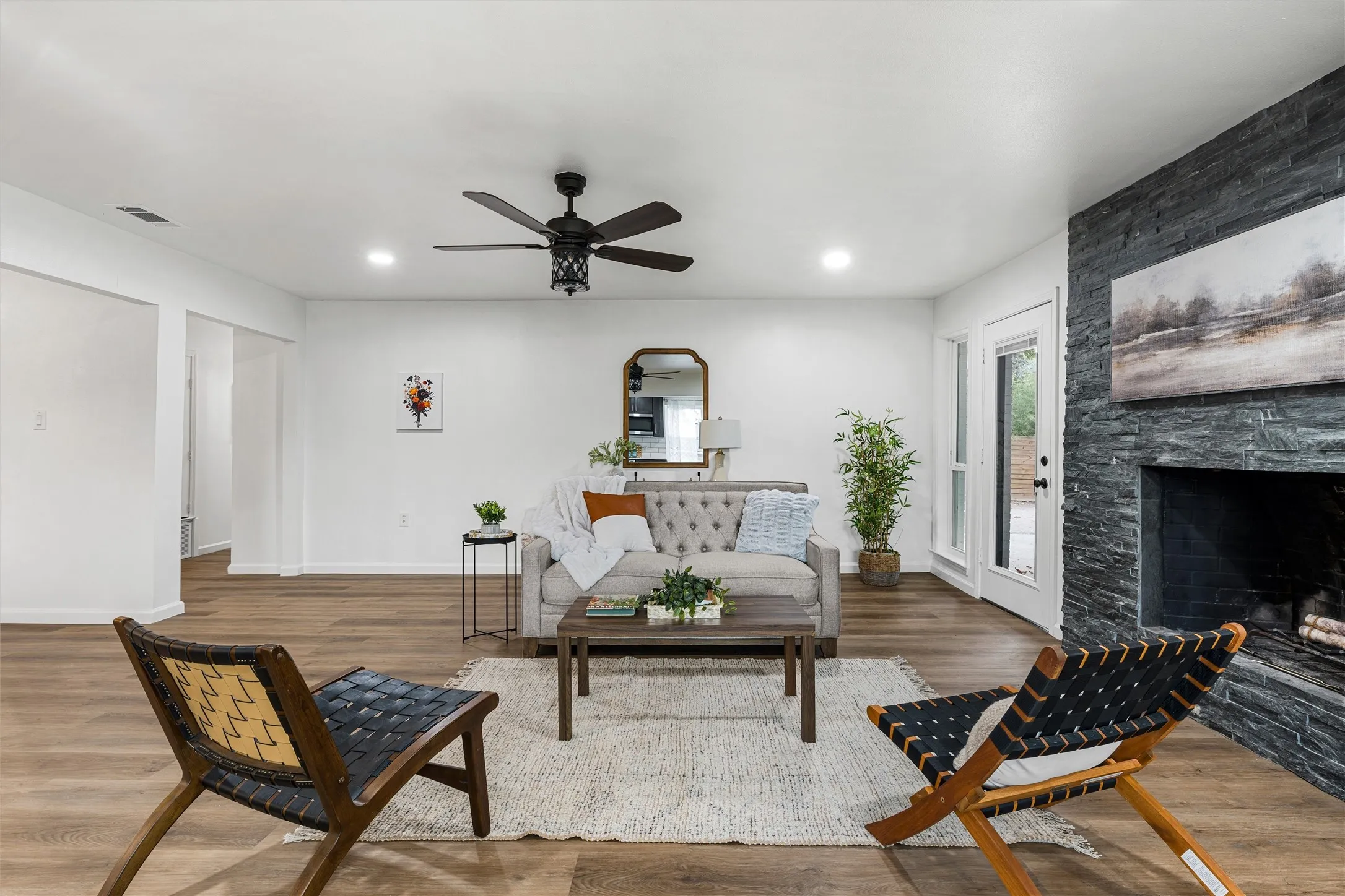 Spacious living area featuring wood-finish flooring, a stacked stone fireplace, recessed lighting, and a ceiling fan