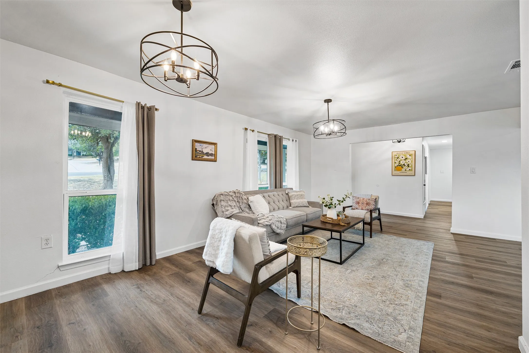 Wood-finish flooring throughout, bright white walls, two contemporary ceiling light fixtures, and a cased opening providing access to another area