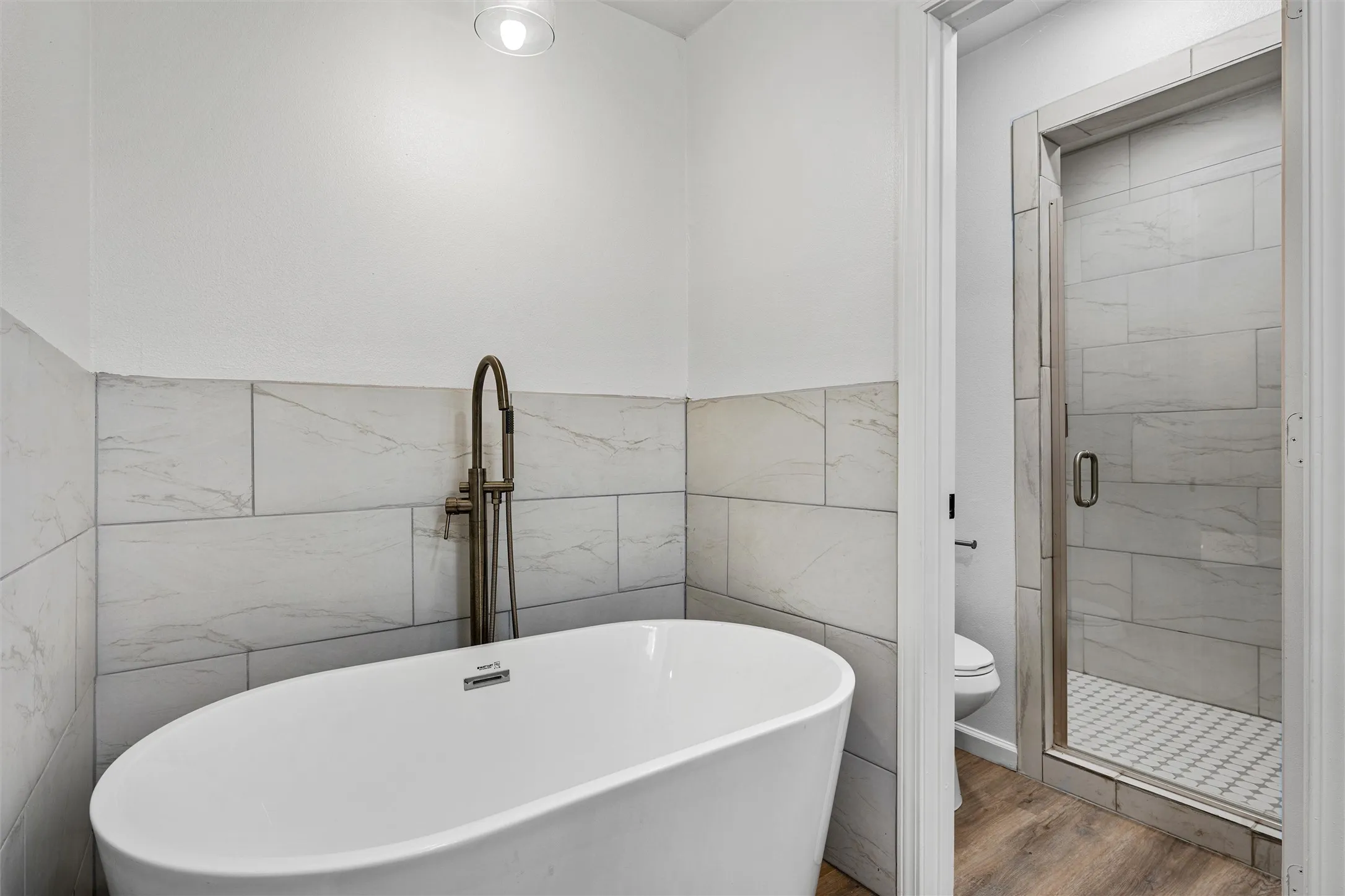 Freestanding soaking tub with floor-mounted fixture, tiled wainscoting, and recessed ceiling lighting