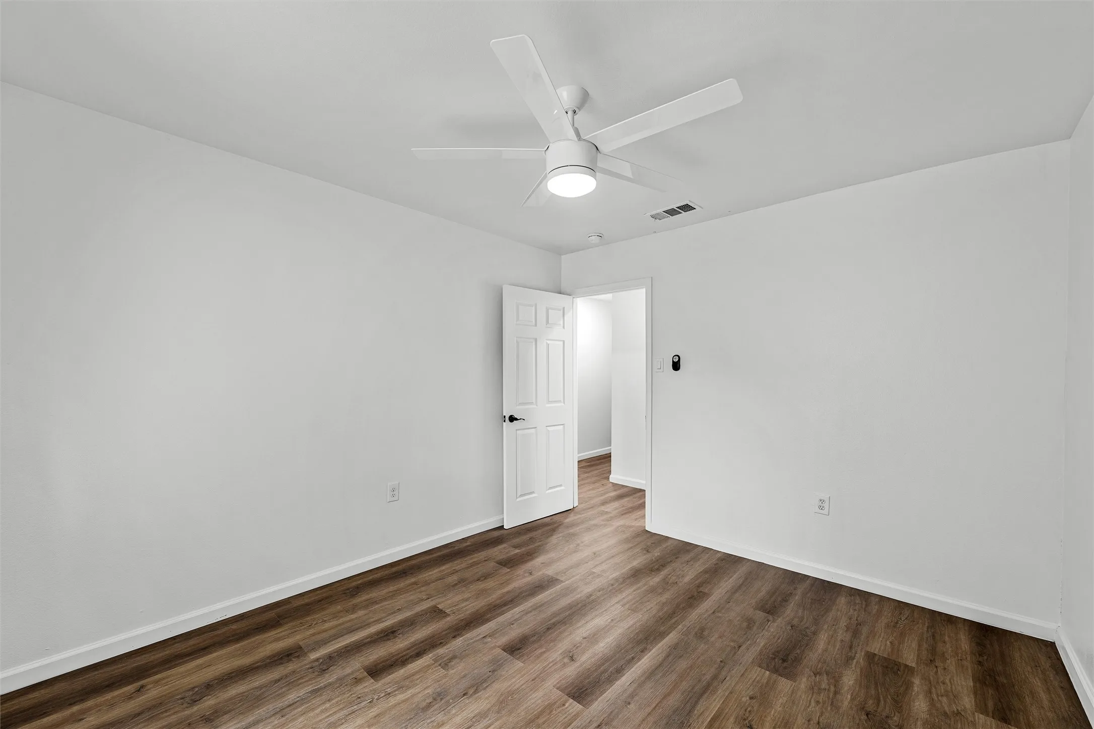 Wood-finish flooring, white walls, and a ceiling fan with integrated lighting
