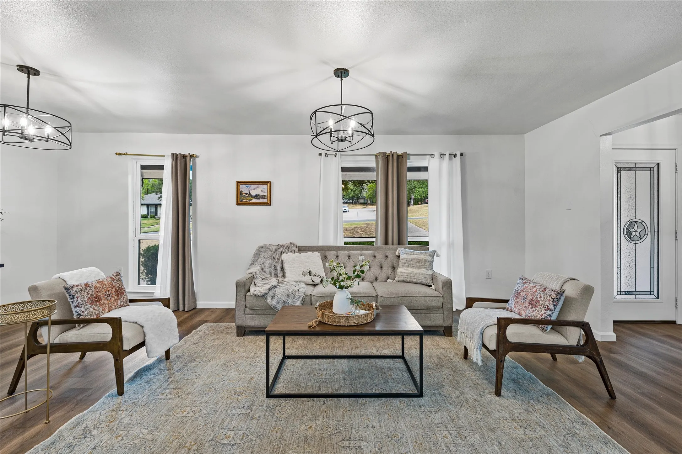 Spacious living area featuring wood-finish flooring, two modern ceiling light fixtures, and white walls