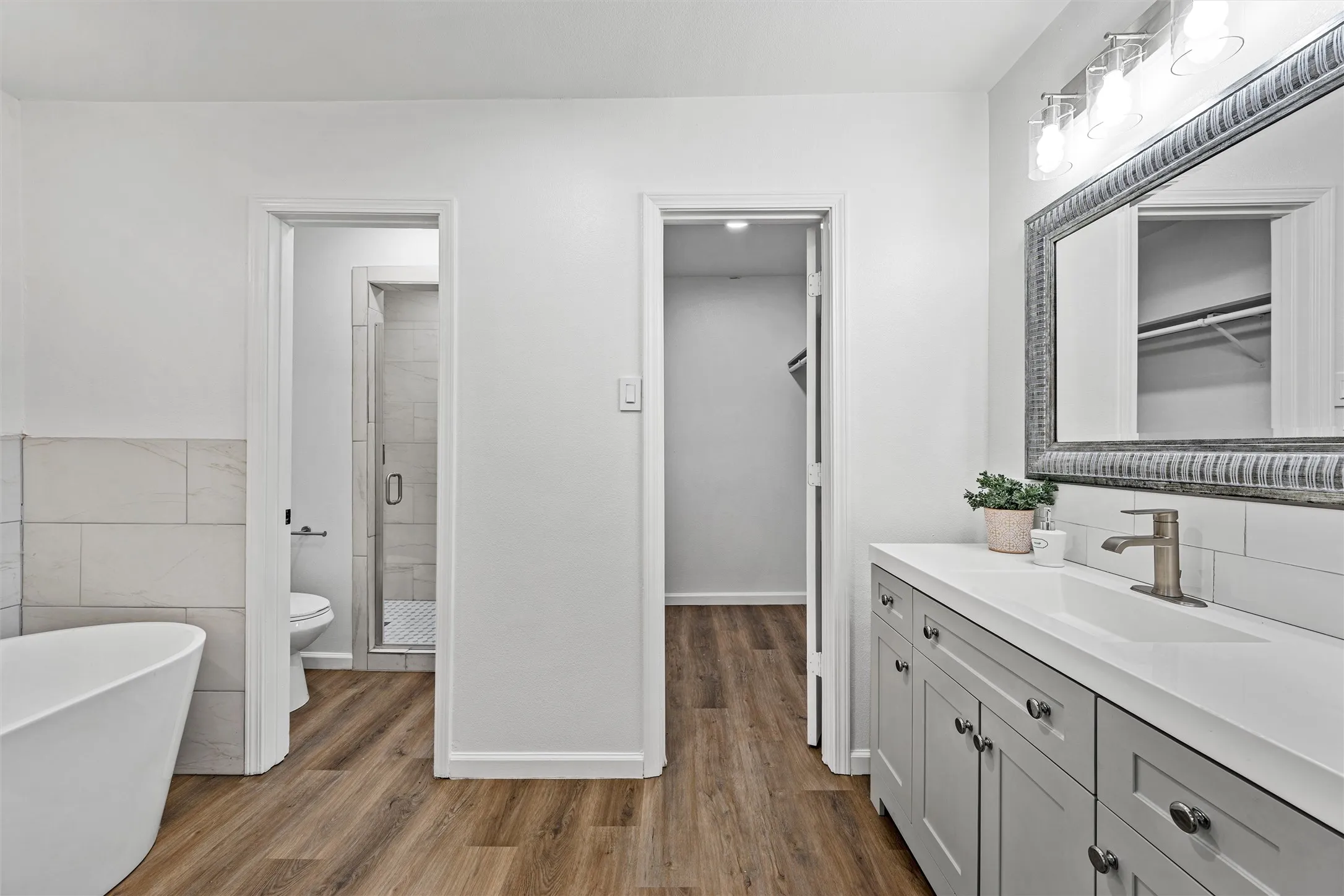 Bathroom featuring a freestanding tub, wood-finish flooring, a vanity with a white countertop, and a walk-in shower with a glass enclosure