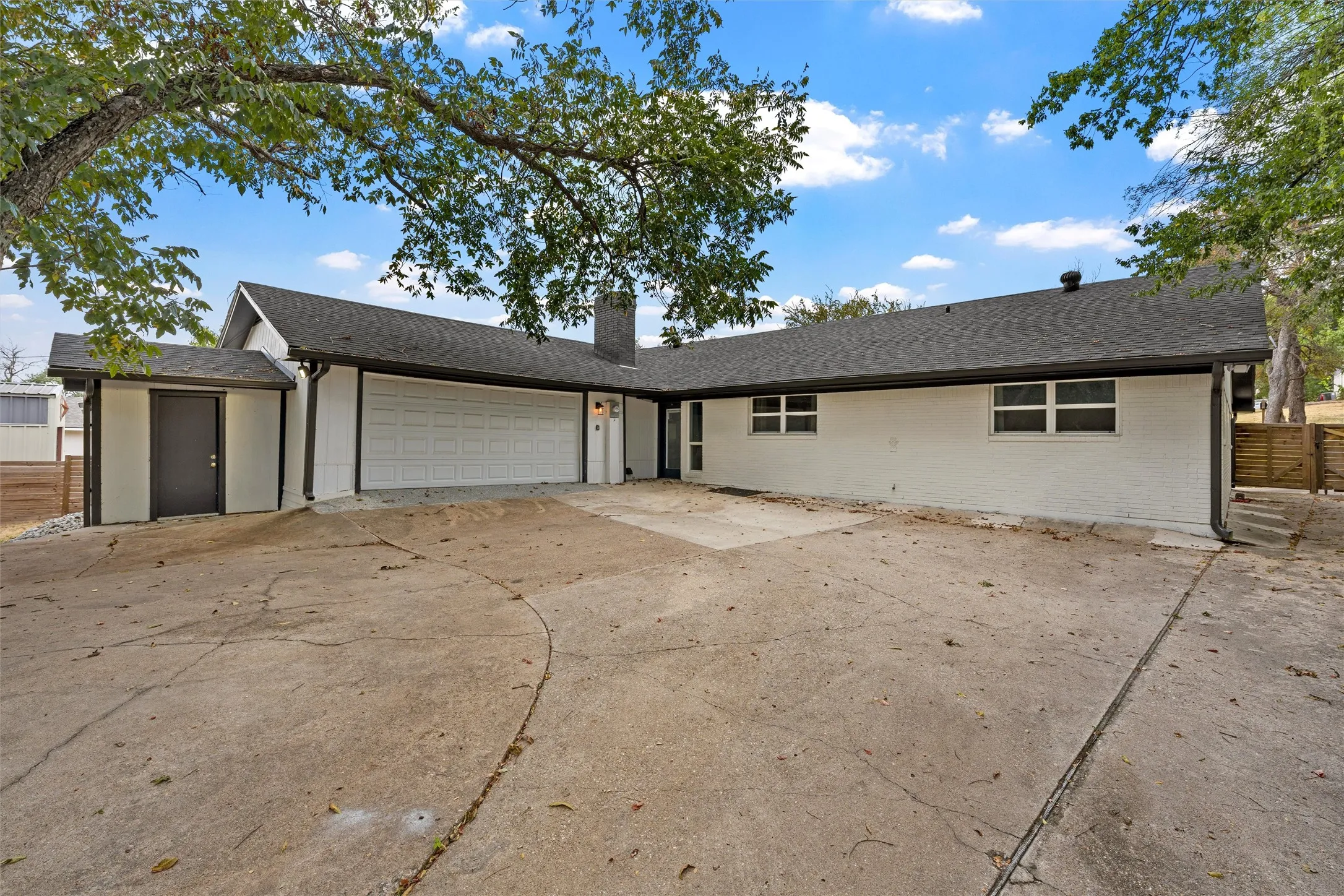 Single-story residence featuring a two-car garage, white painted brick exterior, and a dark shingle roof