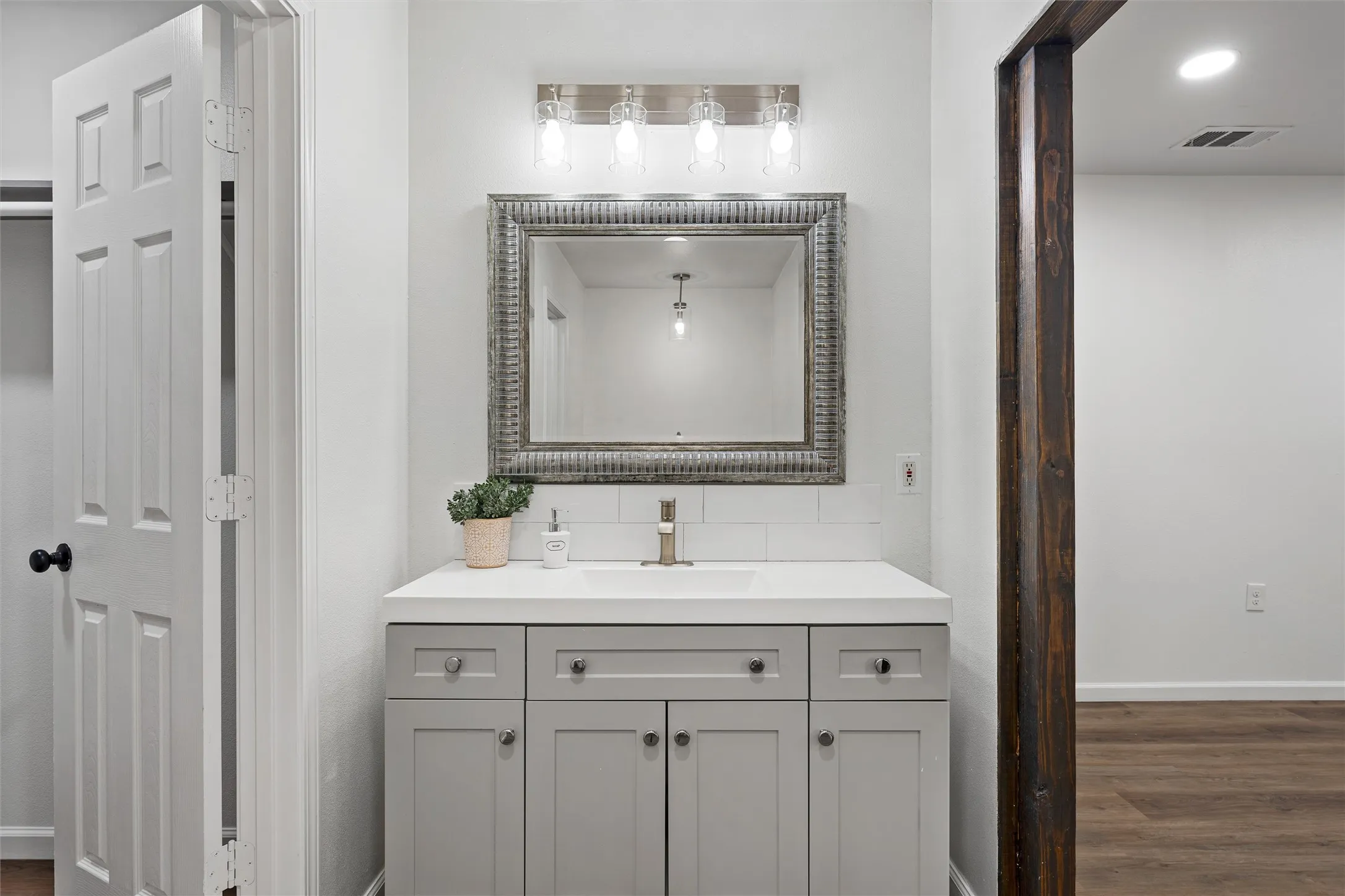 Vanity with light gray shaker-style cabinetry, white countertop, and subway tile backsplash