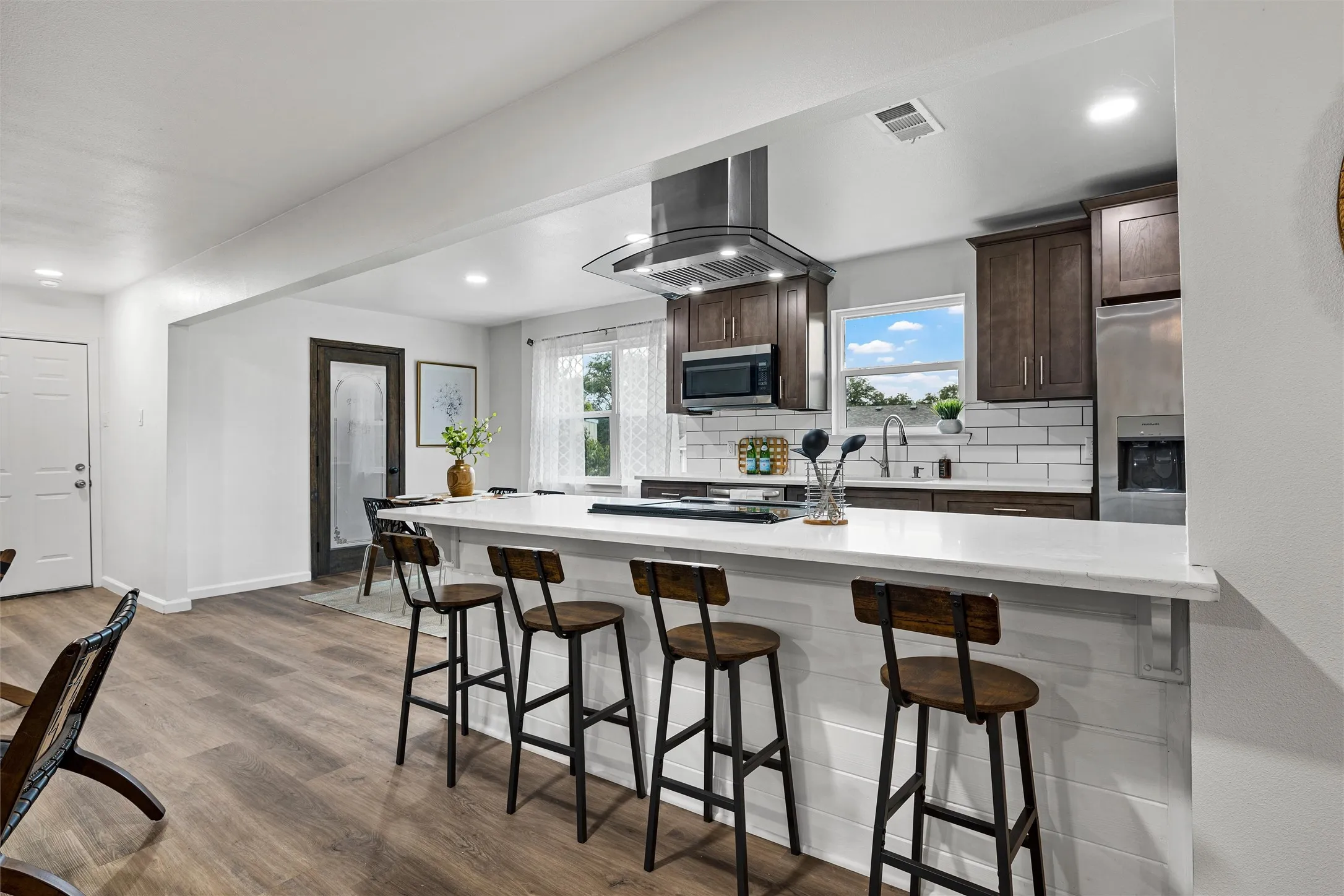 Kitchen featuring dark wood-finish cabinetry, stainless steel appliances, a subway tile backsplash, and a large central island with a white countertop