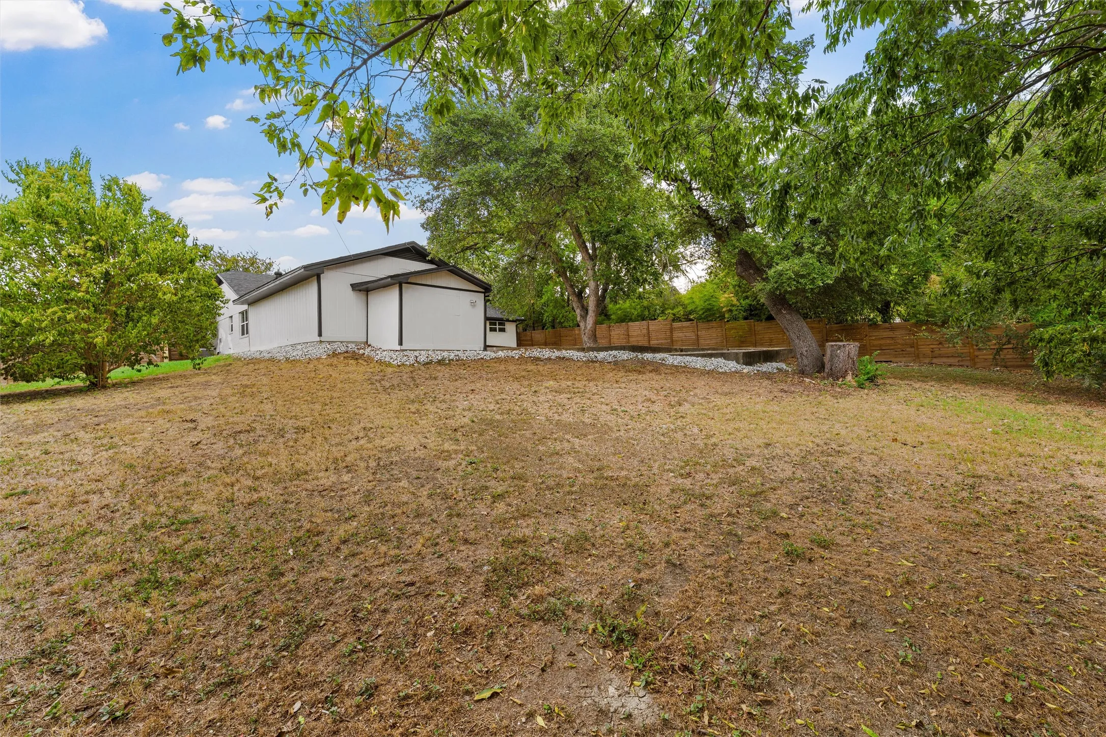 Expansive property featuring a contemporary-style home, mature trees, and a wooden fence