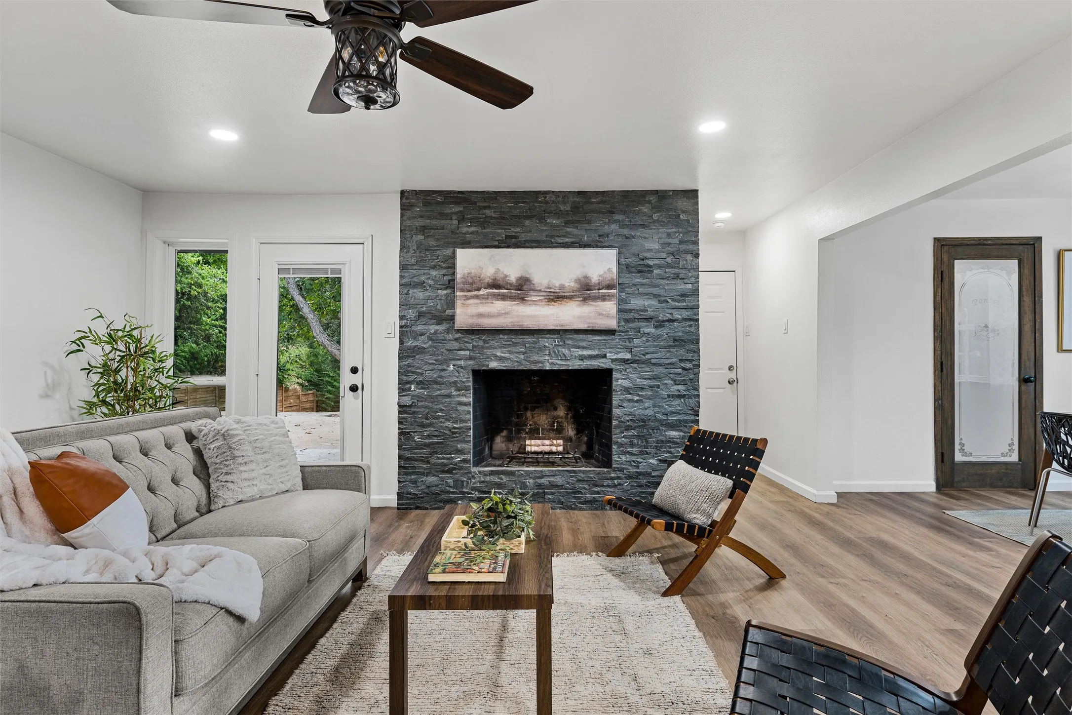 Stacked stone fireplace, wood-finish flooring, recessed lighting, ceiling fan, and exterior access