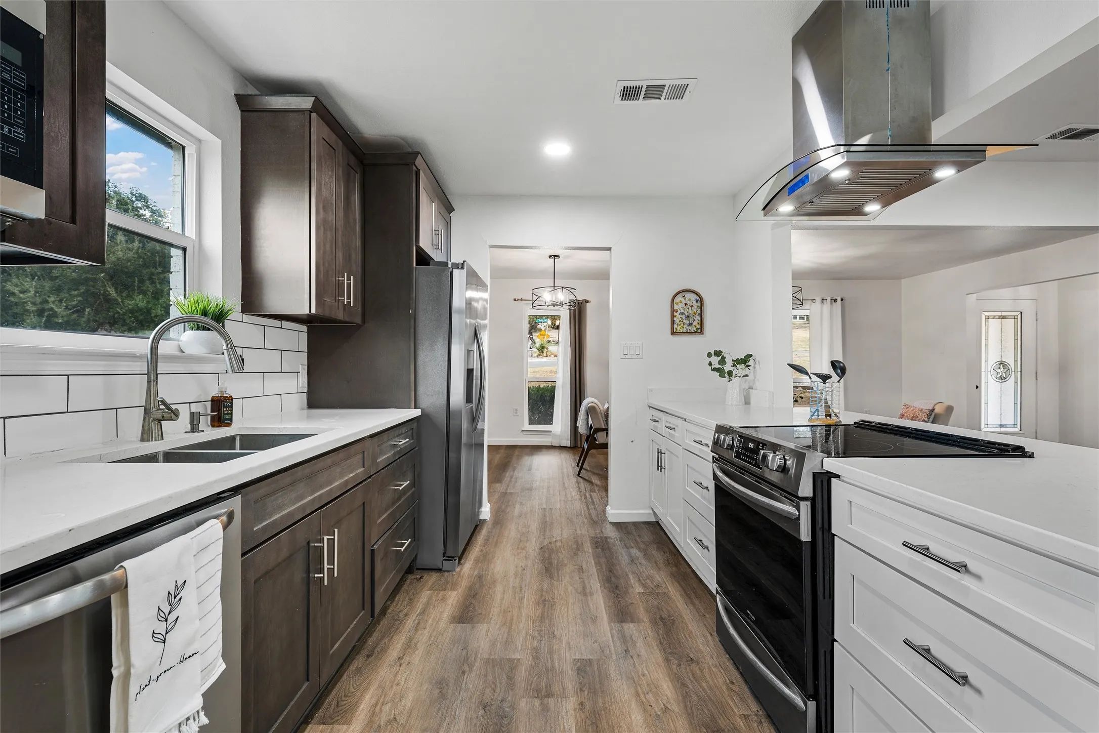 Modern kitchen featuring wood-finish flooring, white countertops, two-tone cabinetry, a stainless steel sink, and a built-in electric range with an overhead vent hood