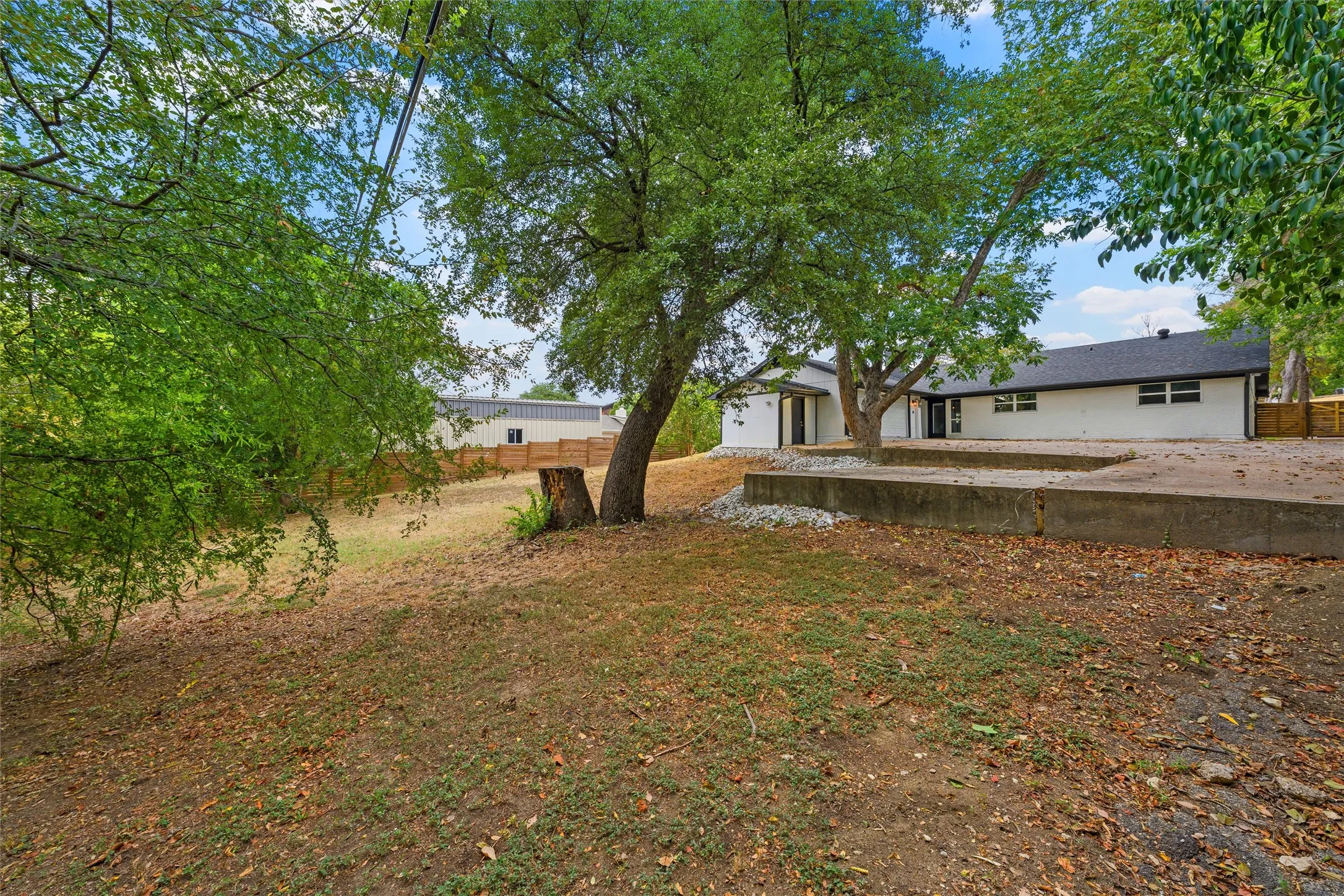Expansive backyard featuring mature trees, a concrete patio, and a sloped terrain