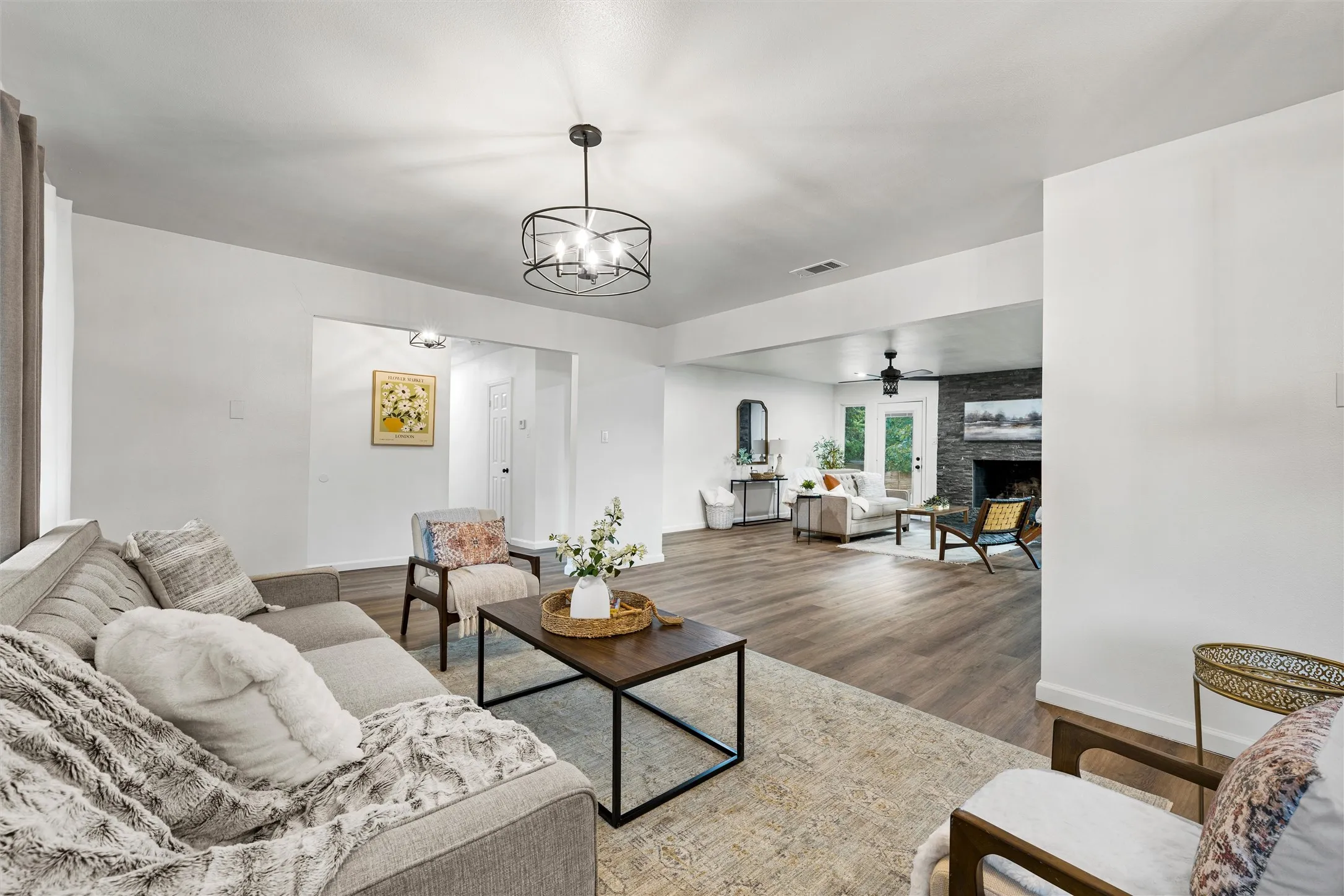 Expansive living area featuring wood-finish flooring, a contemporary ceiling light fixture, and a stone-clad fireplace