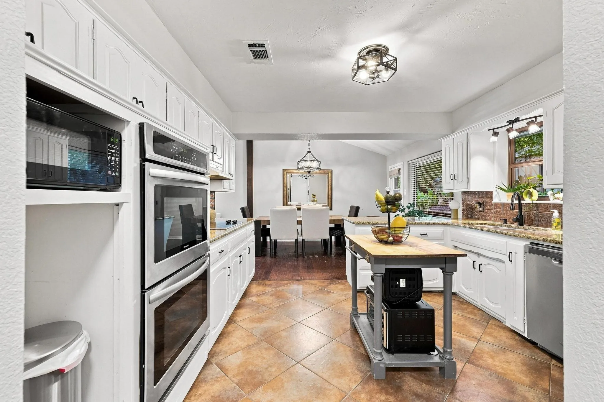 Kitchen featuring white cabinetry, stainless steel double ovens, tile flooring, granite countertops, and an island with a wood-finish top