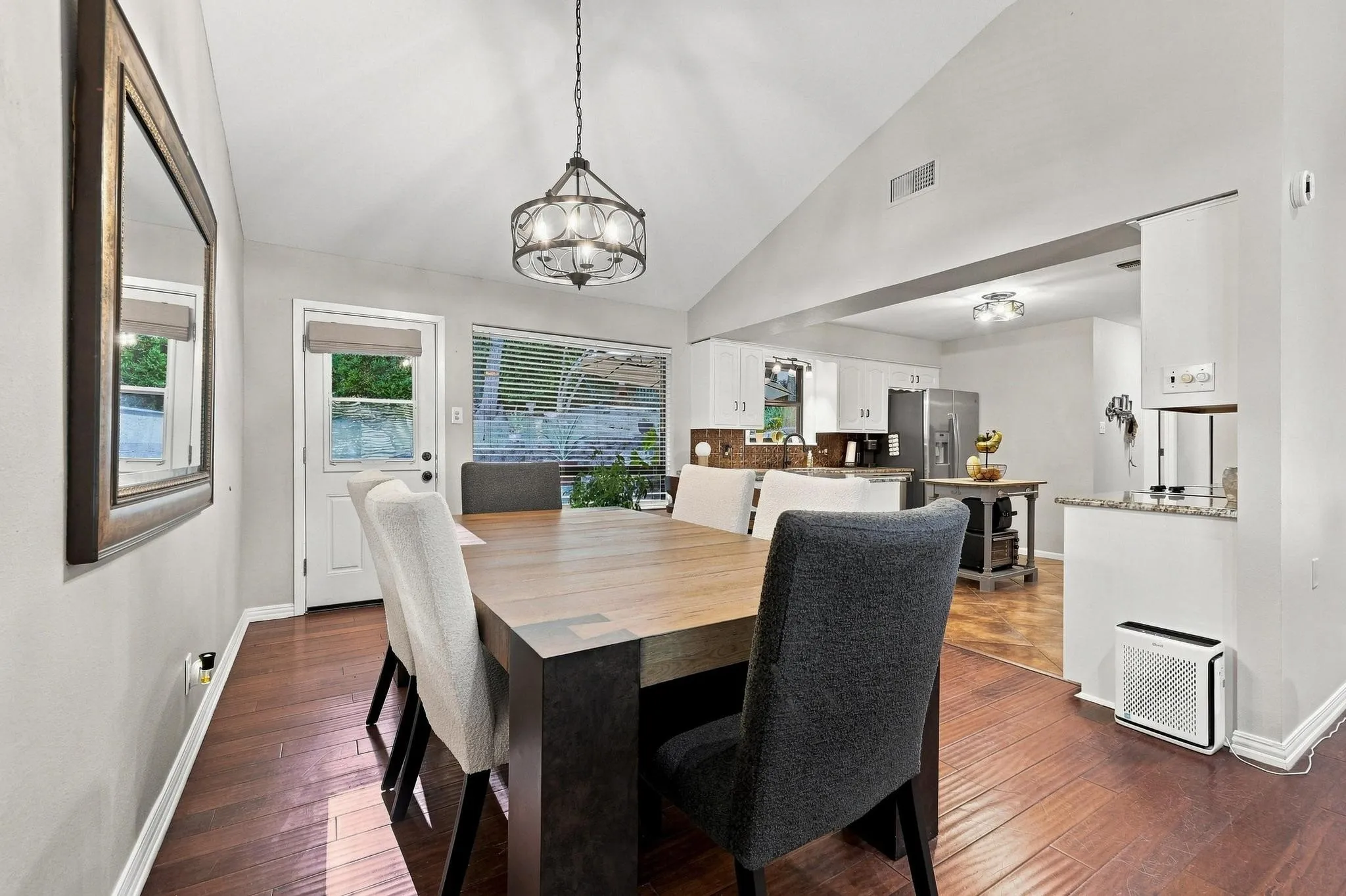Vaulted ceiling, wood-finish flooring, contemporary chandelier, kitchen pass-through, and a white paneled door with glass insert